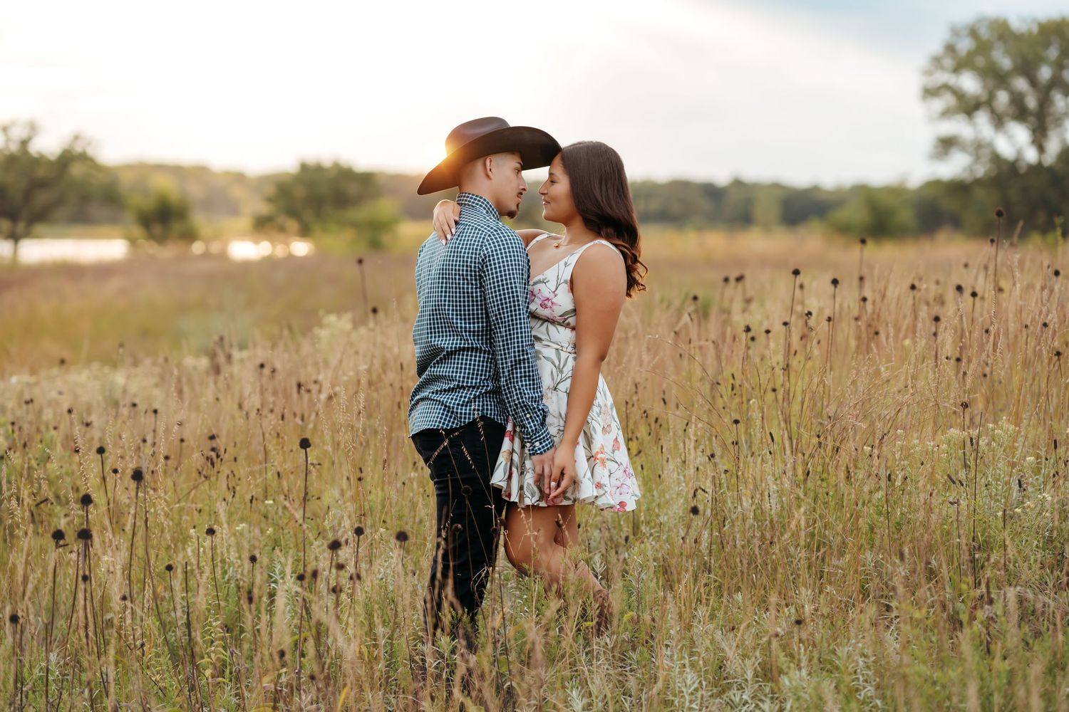 A couple embraces in a golden wildflower field during sunset creating a romantic silhouette against the warm sky.