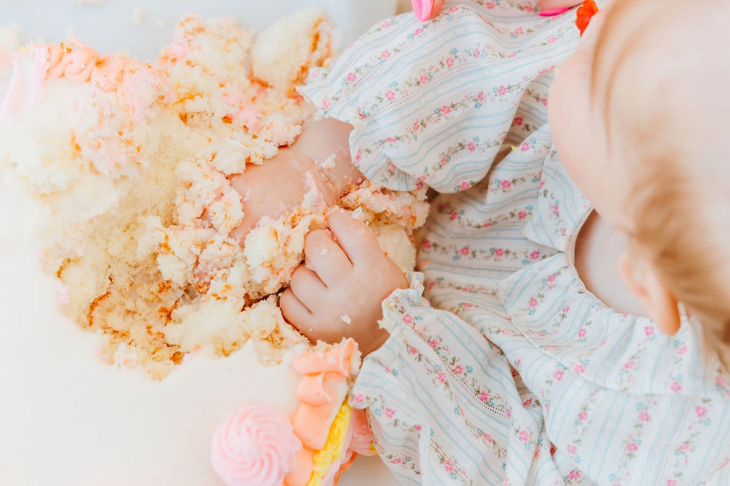 Hands smashing and crumbling a pink and orange birthday cake into small pieces on a white surface.