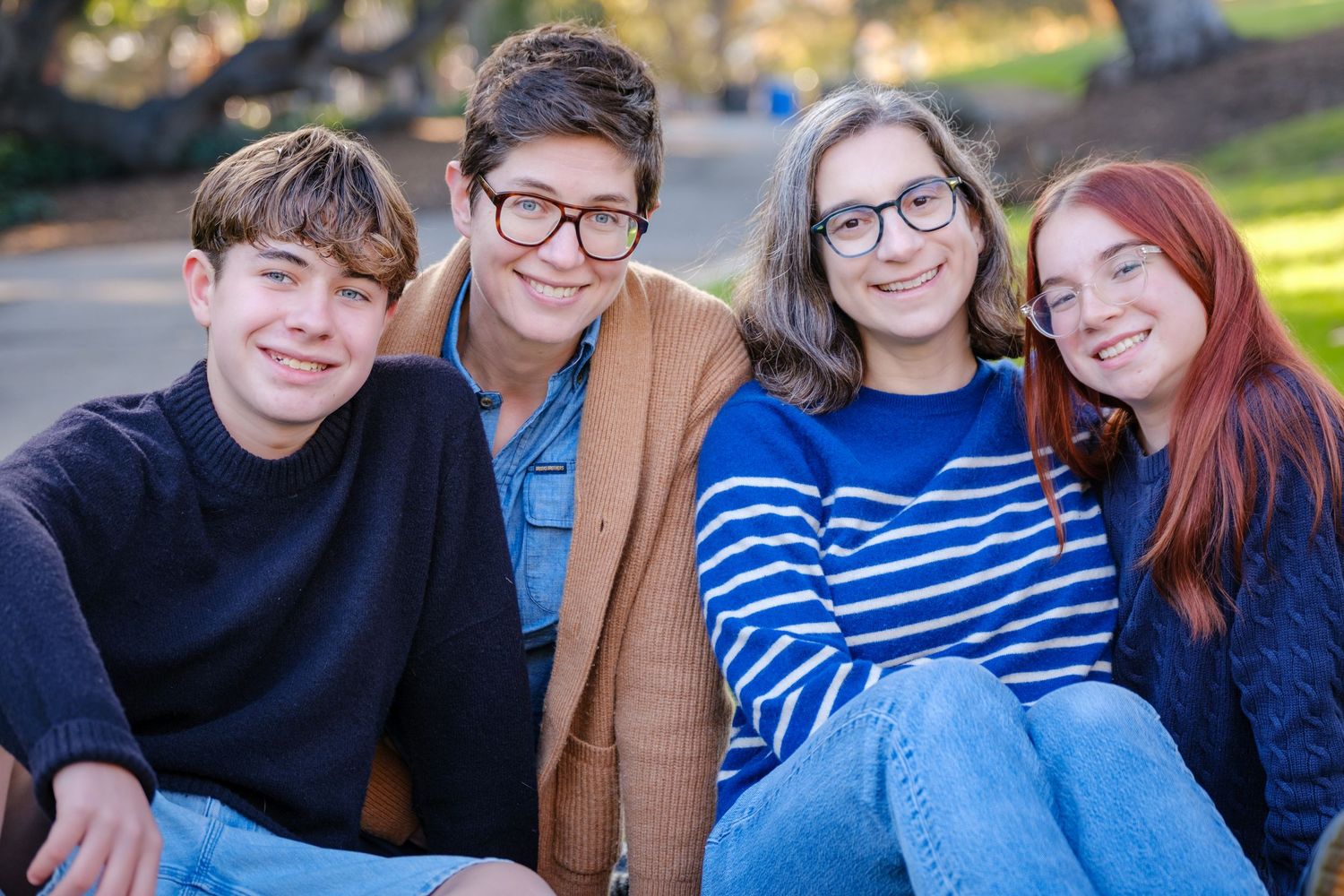 Four friends sitting together outdoors smiling at camera on a sunny autumn day.