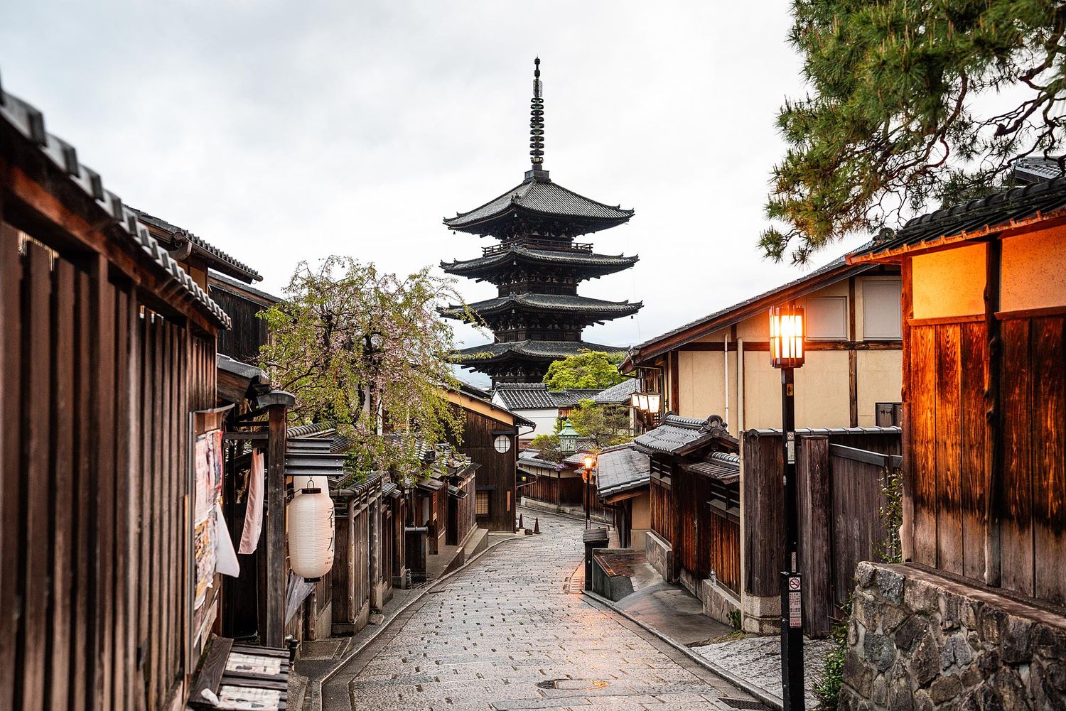 Historic cobblestone street in Kyoto's Gion district with traditional wooden buildings and pagoda tower at dusk.