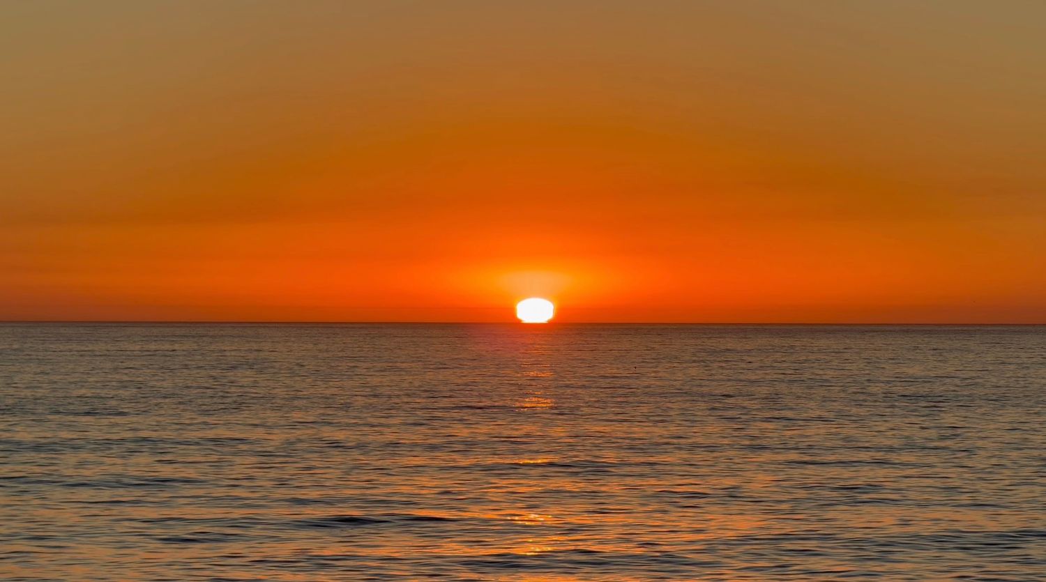 A vibrant orange sunset casts golden reflections across the calm ocean waters.