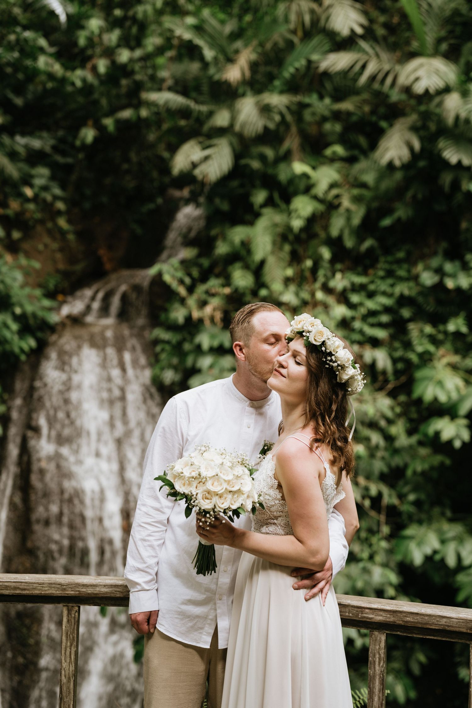 Romantic moment captured on wooden deck with tropical waterfall backdrop.