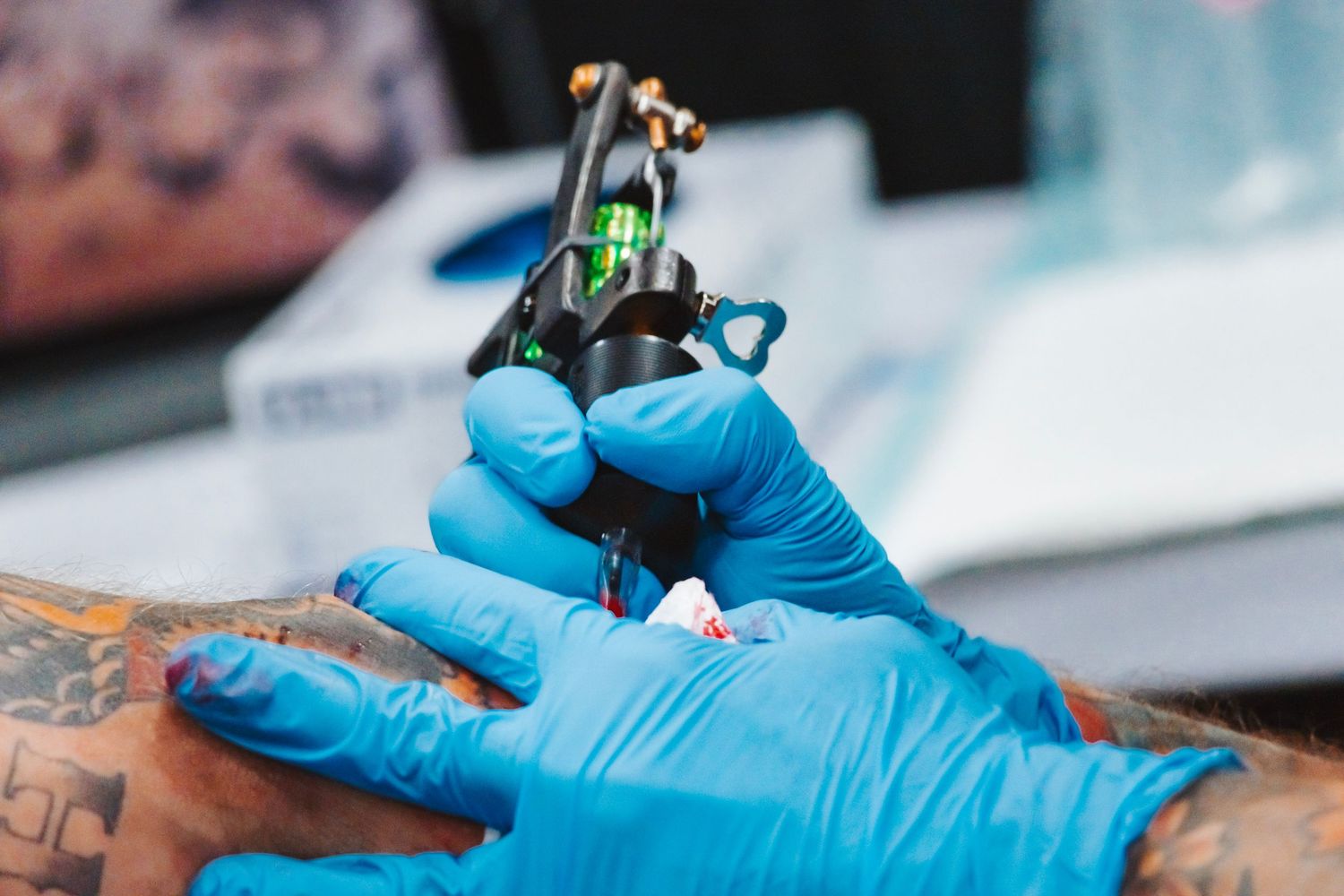 Close-up of hands wearing blue medical gloves performing a tattoo procedure with professional equipment.