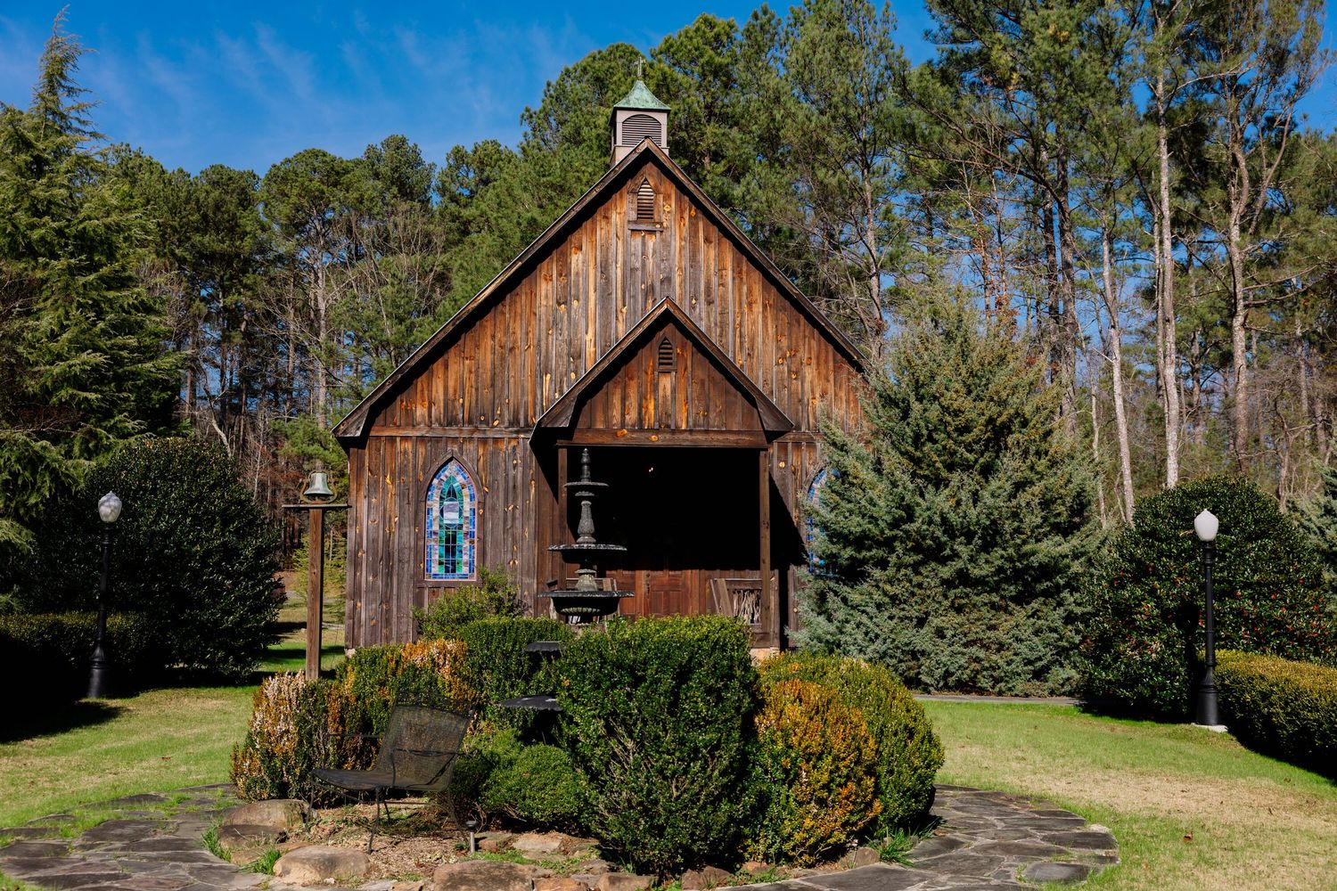 A rustic wooden barn with weathered siding stands among evergreen trees on a sunny day.