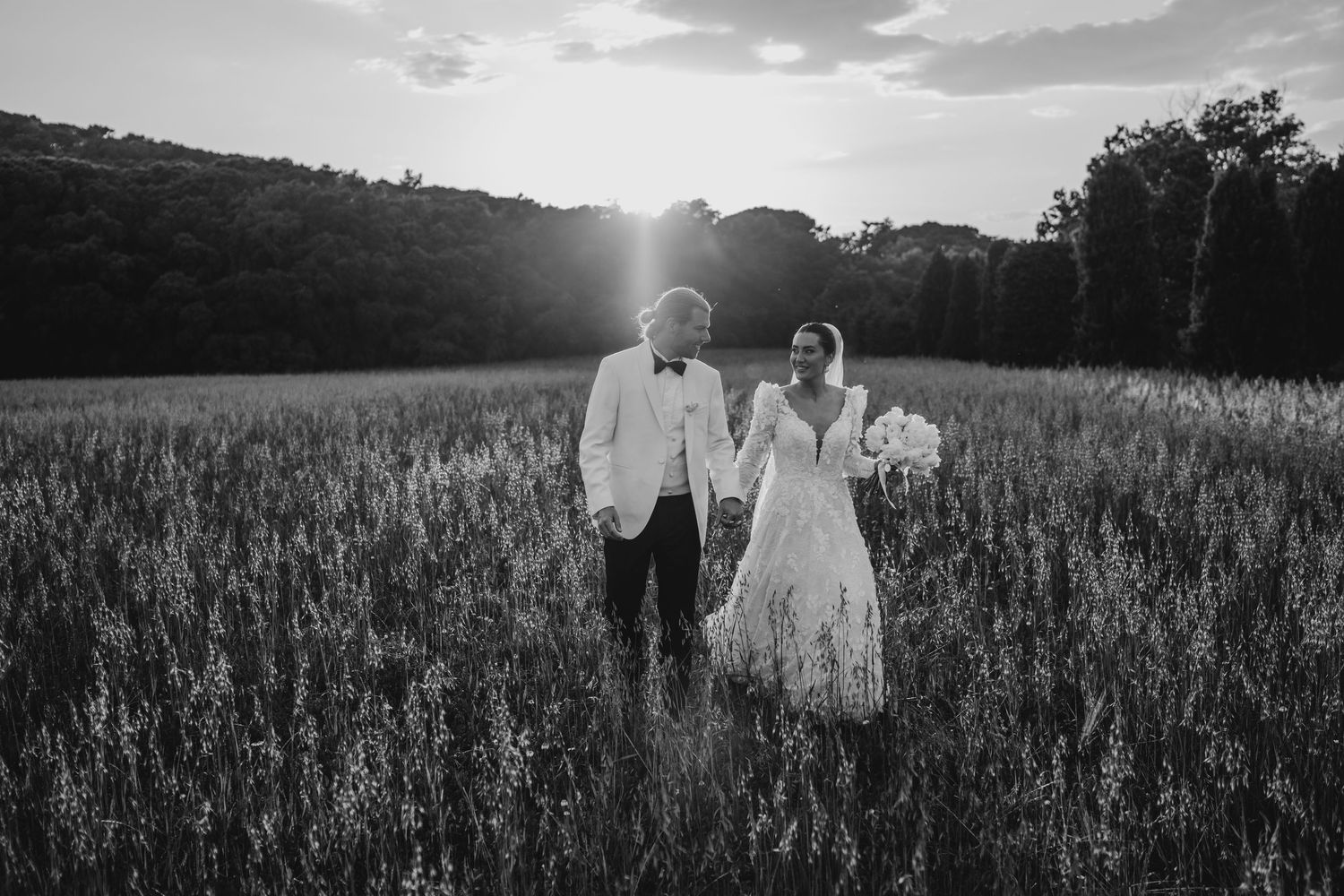 A couple walks down a garden path between tall hedges during a golden sunset hour.