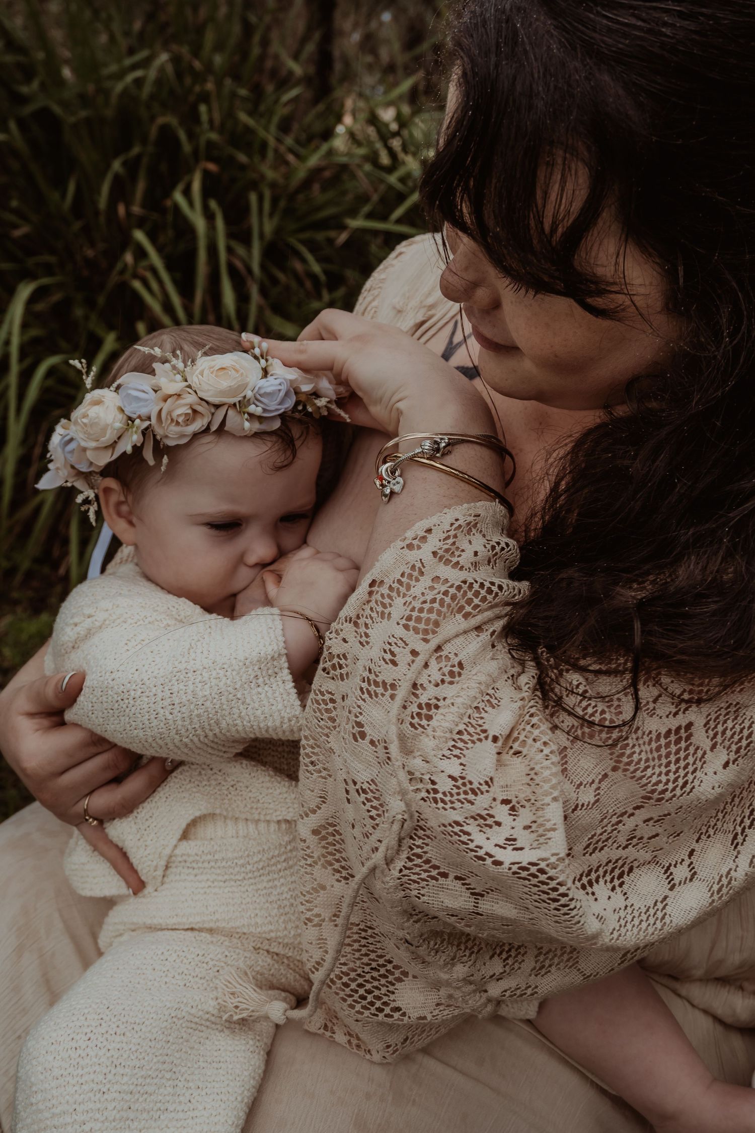 Baby in white sweater and denim resting on ornate white wicker furniture.