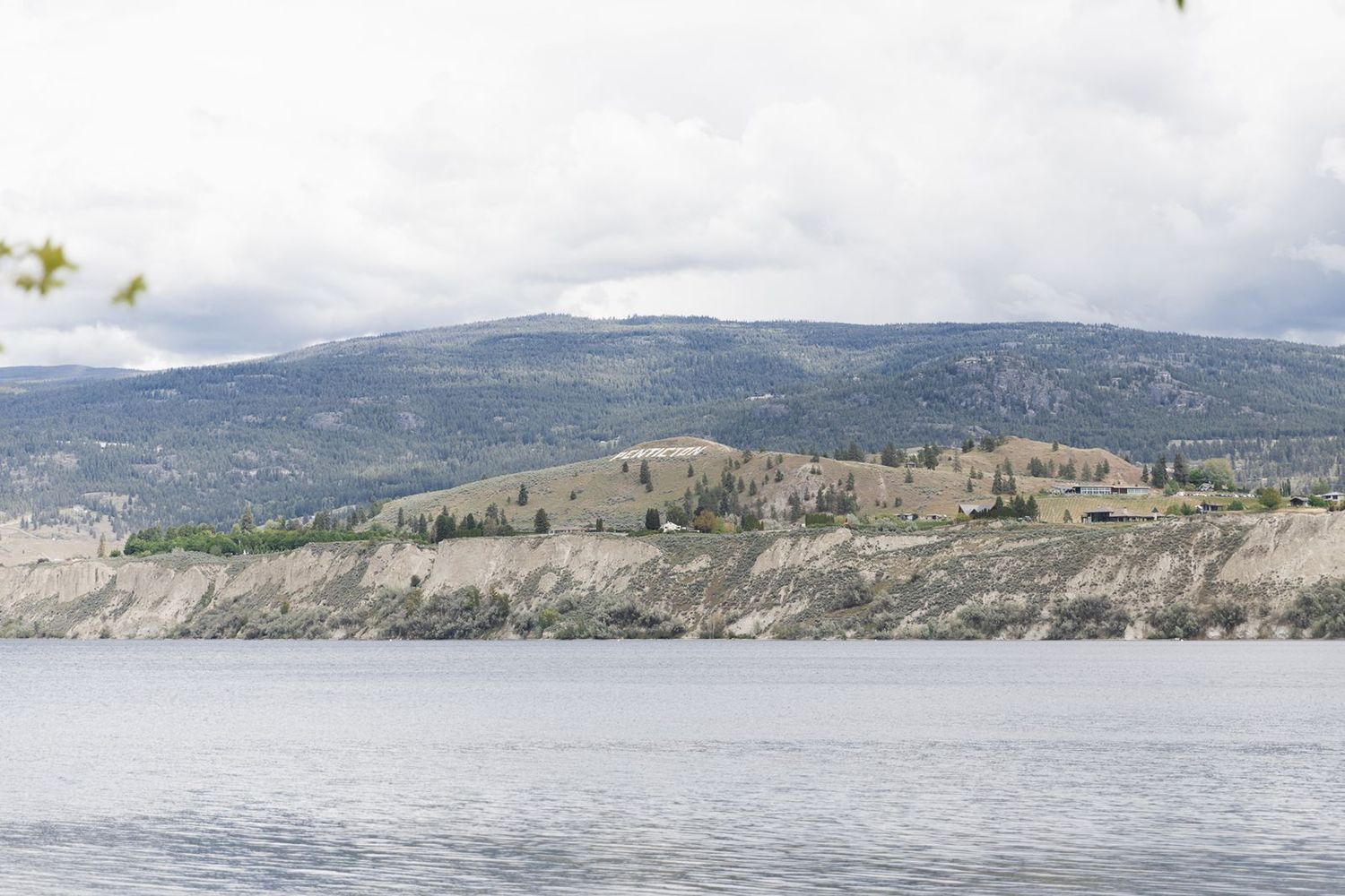 Scenic landscape view of rocky cliffs and mountains reflected in calm lake waters under cloudy sky.