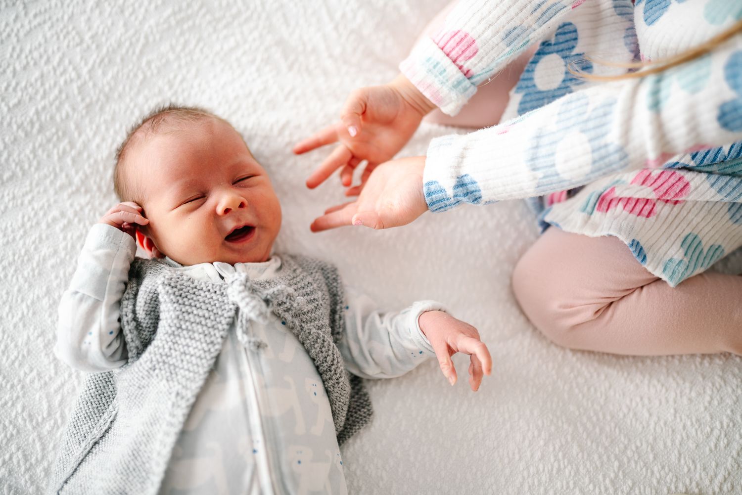 Elder sister touching a sleeping newborn baby wearing a cozy gray sweater during a family newborn photo session in Melbourne.