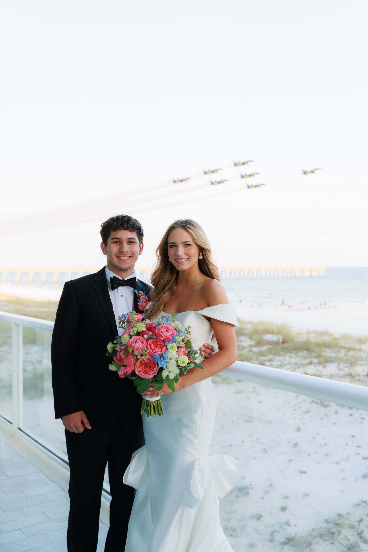 Newly married couple walking along brick path by white picket fence under tree canopy.