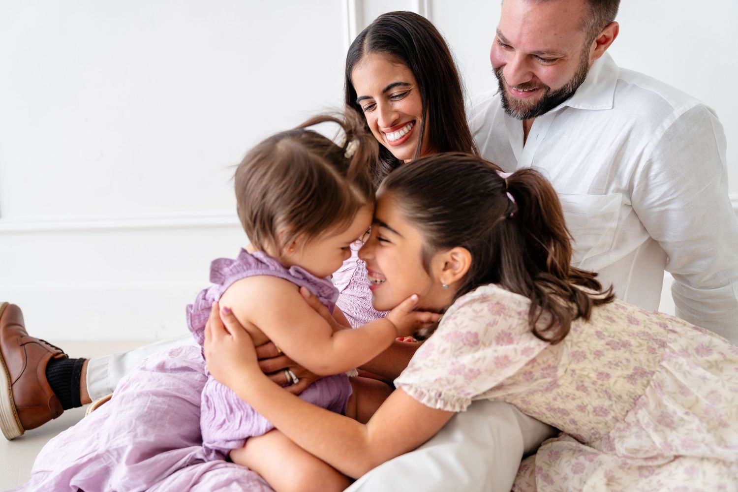 Happy family members embrace together while playing and laughing on white bed.