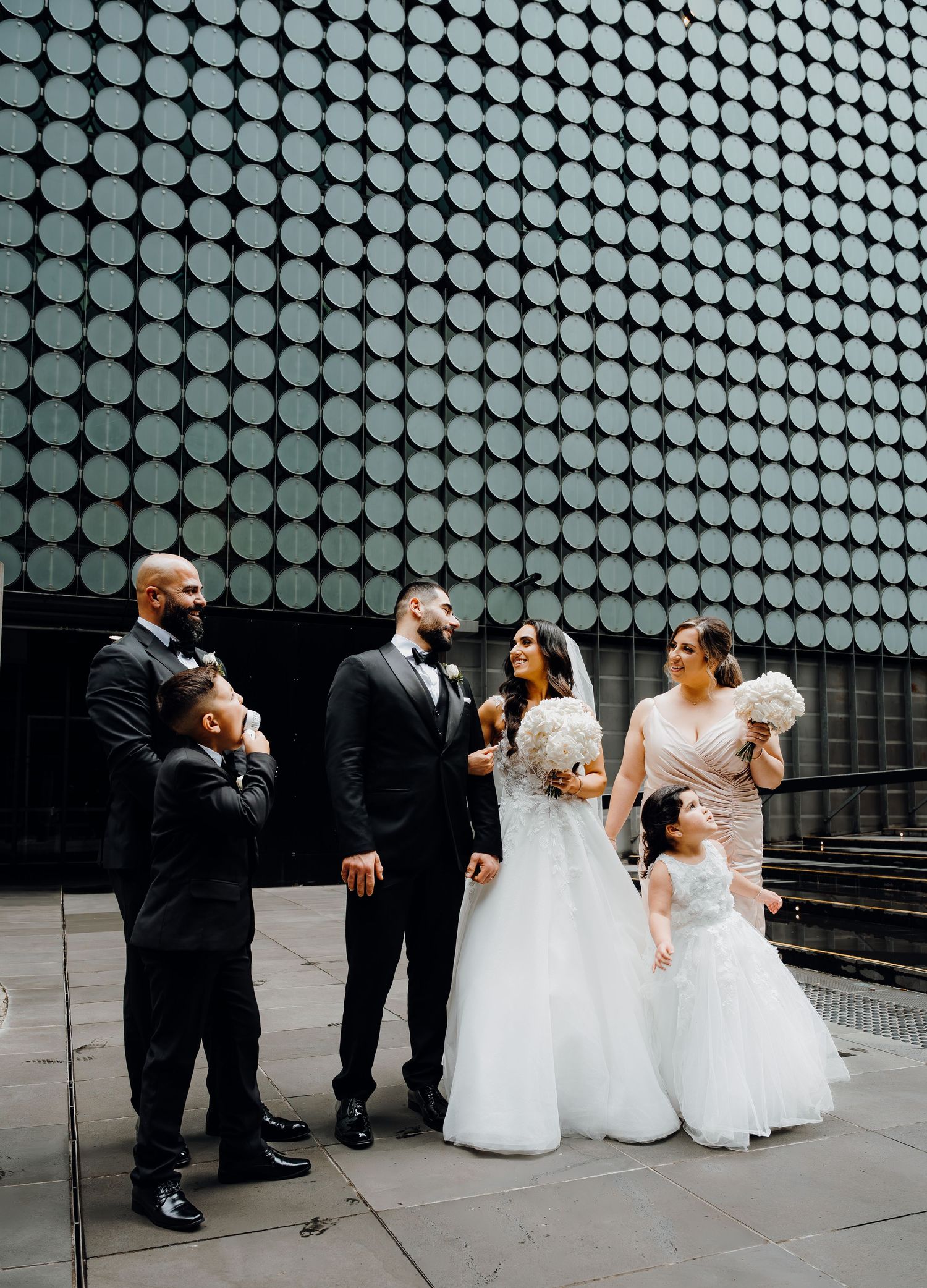 A wedding party poses casually against a modern architectural wall with circular dot pattern background in black and white.