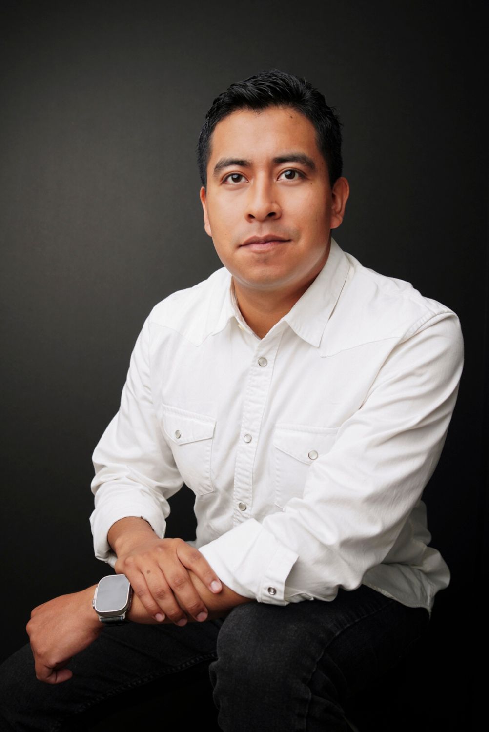 Professional in a light blue button-down shirt poses with crossed arms in an office setting.