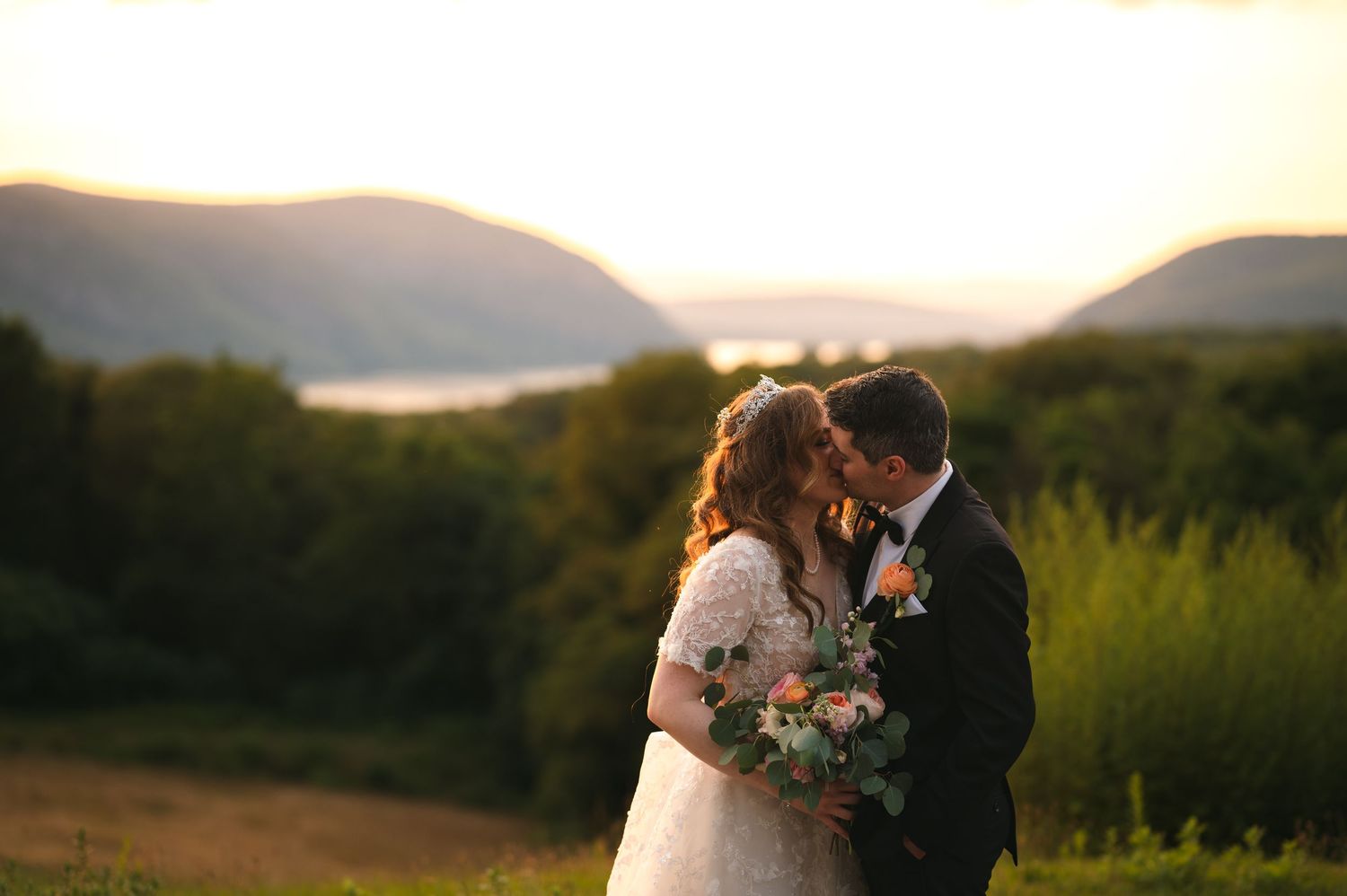 A beautiful outdoor wedding ceremony taking place in a green garden setting with guests seated in white chairs and floral arch.
