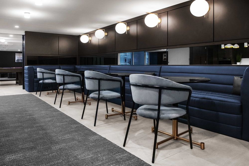 Modern office lounge area with blue banquette seating and pendant lights mounted along the wall.
