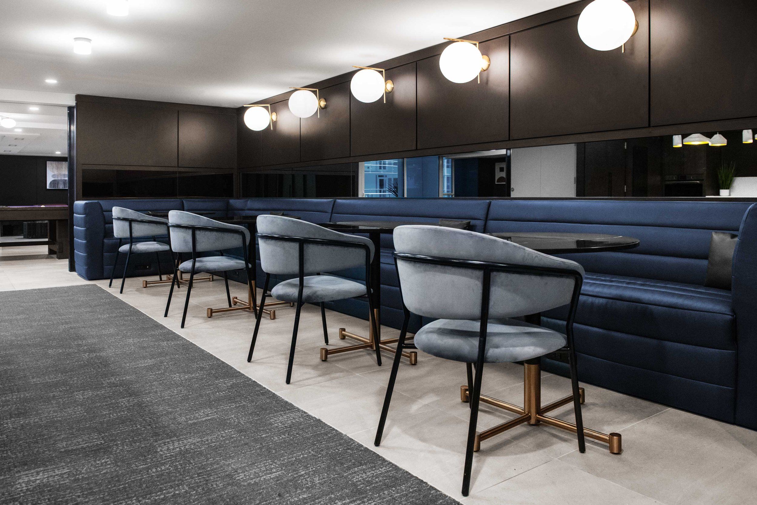 Modern office lounge area with blue banquette seating and pendant lights mounted along the wall.