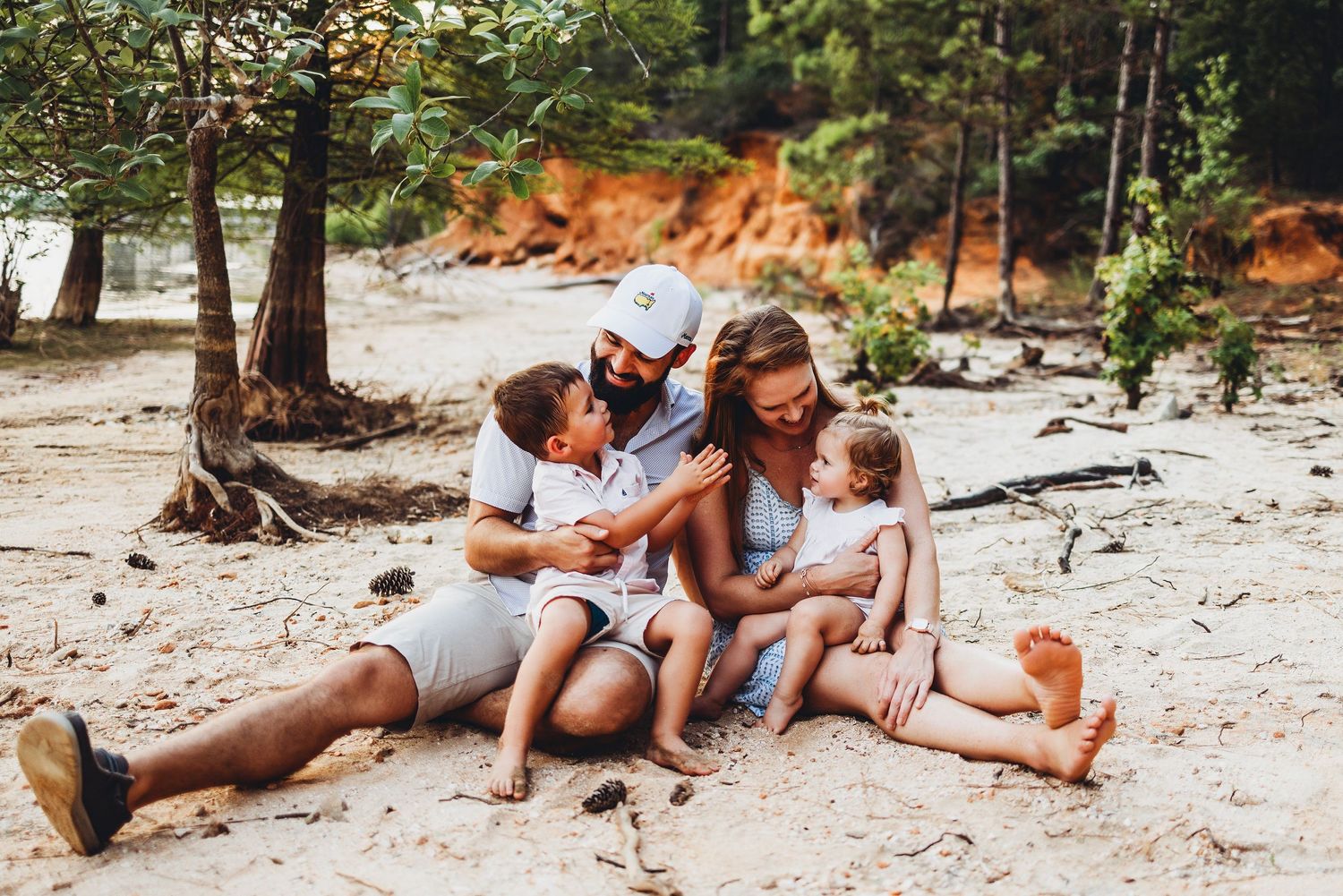 Family relaxing together on sandy beach surrounded by trees.