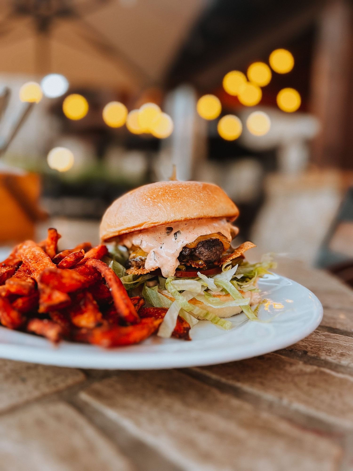 Gourmet burger served with sweet potato fries on white plate in restaurant setting.