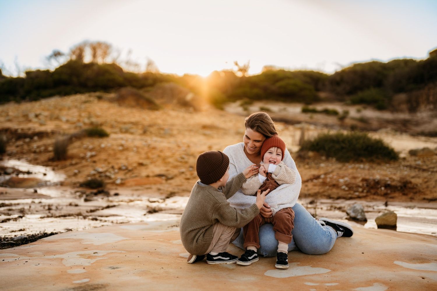 Mother laughs and cuddles children in winter photoshoot wearing knits in earthy colours