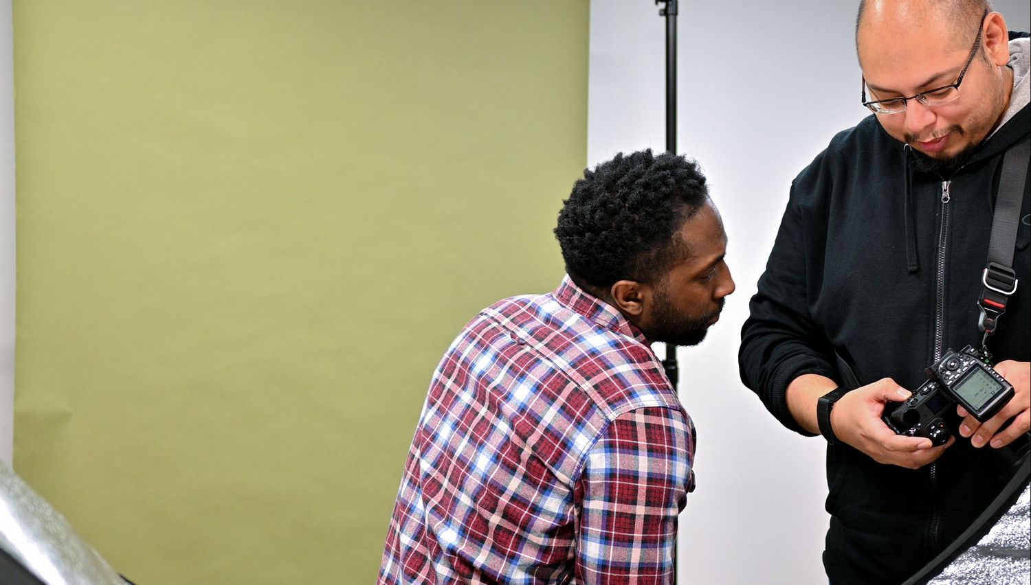 Photographer reviewing camera settings with a man in a plaid shirt in a photography studio.