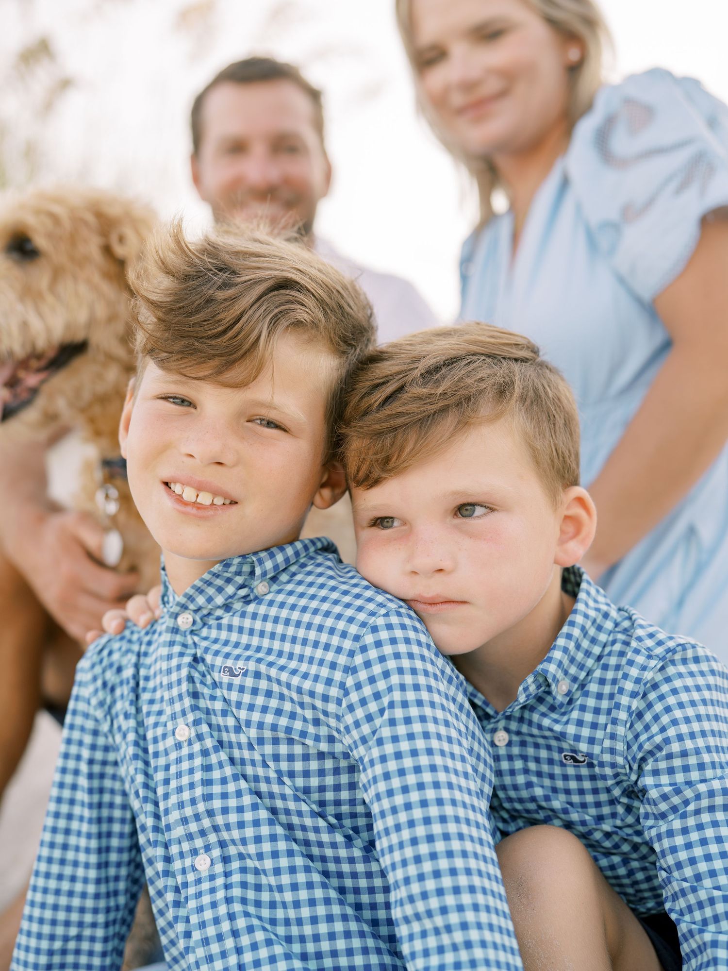 Family dressed in blue and white sits together with their golden retriever outdoors.
