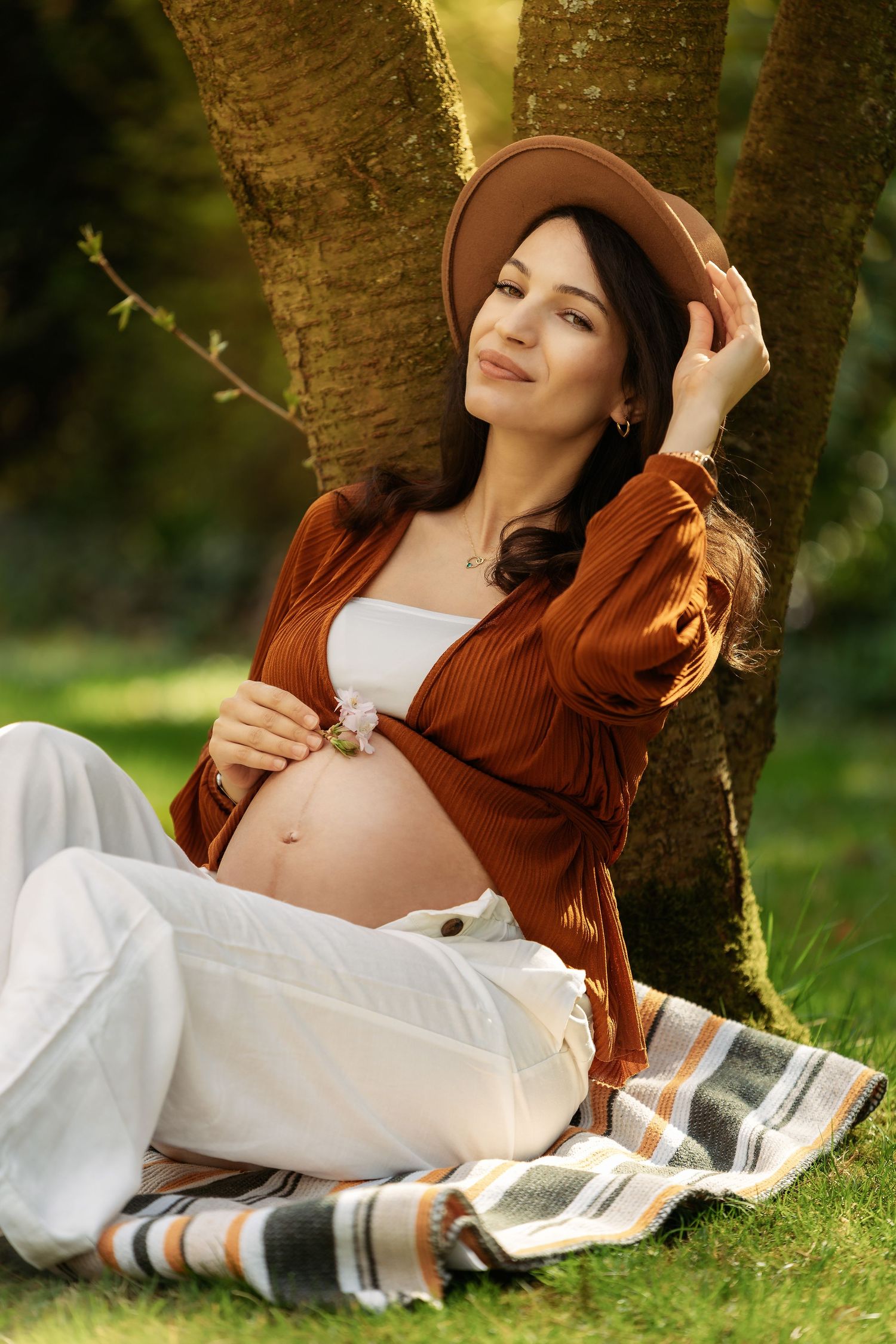 Maternity photo session showing a relaxed pose under a tree in autumn clothing.