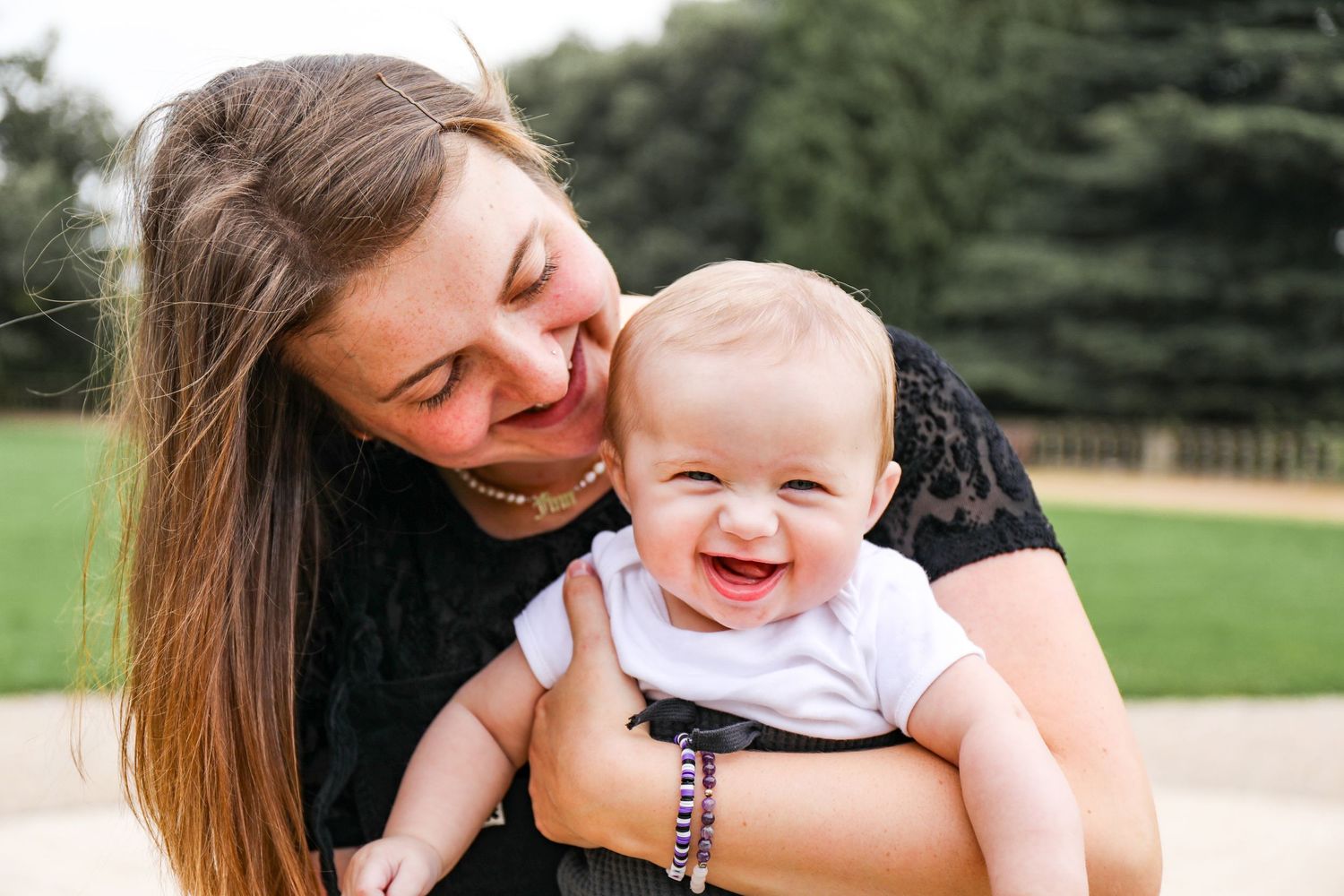 A happy baby in a white onesie smiles while being held outdoors during family photoshoot in Nottingham