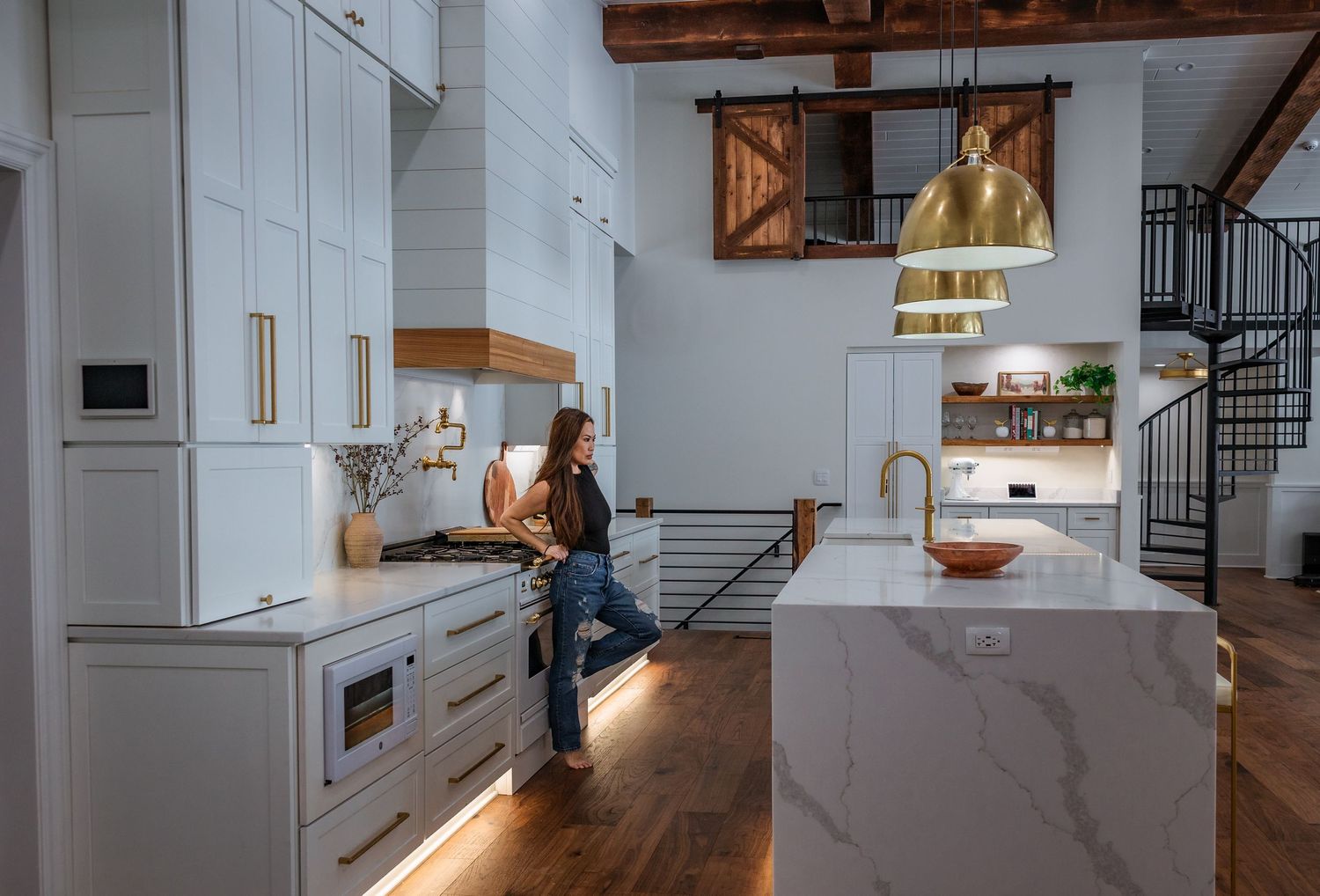 Contemporary kitchen interior with marble island and wooden beam accents in warm lighting.