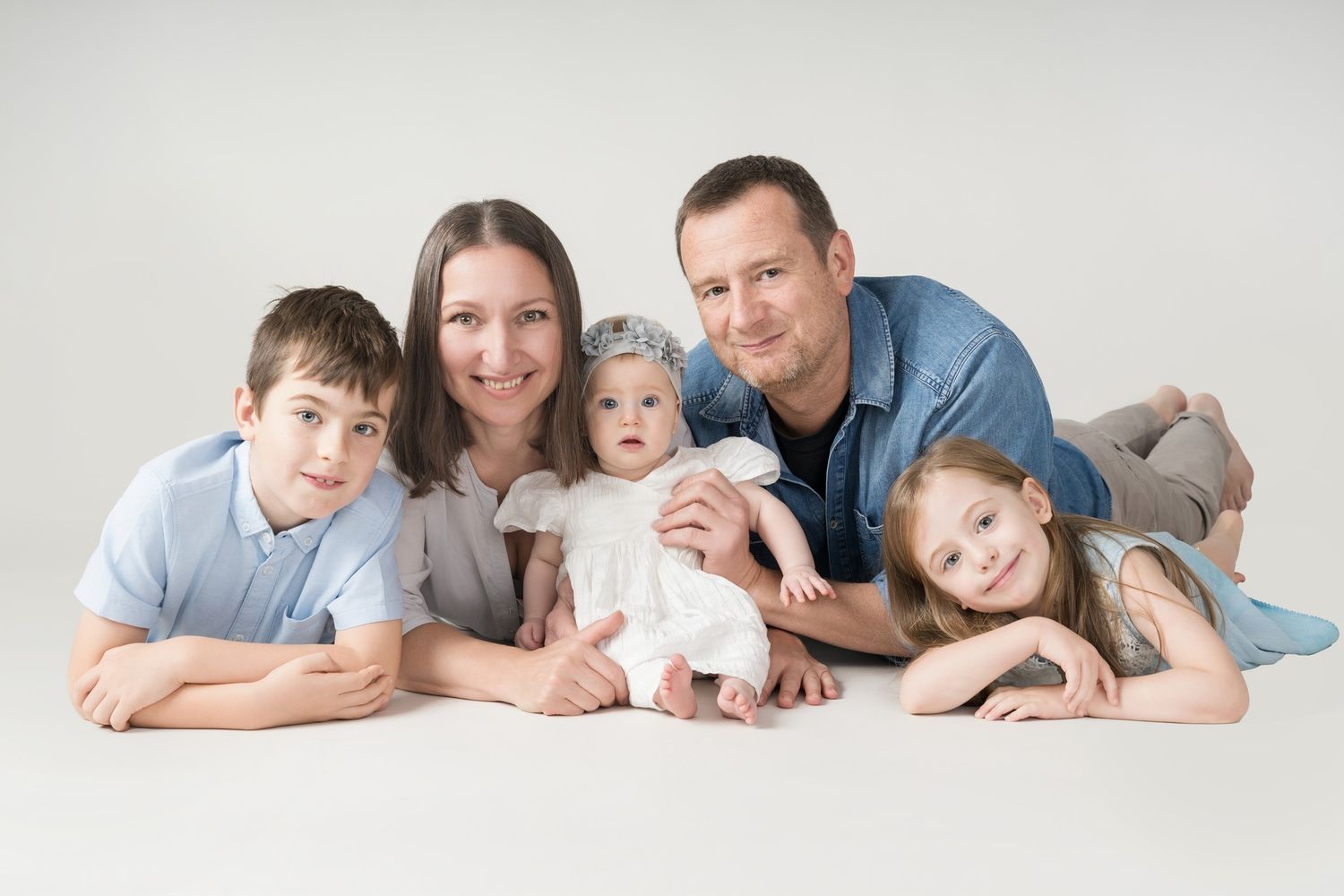 A family group lying together on a light background wearing coordinated blue and white clothing.