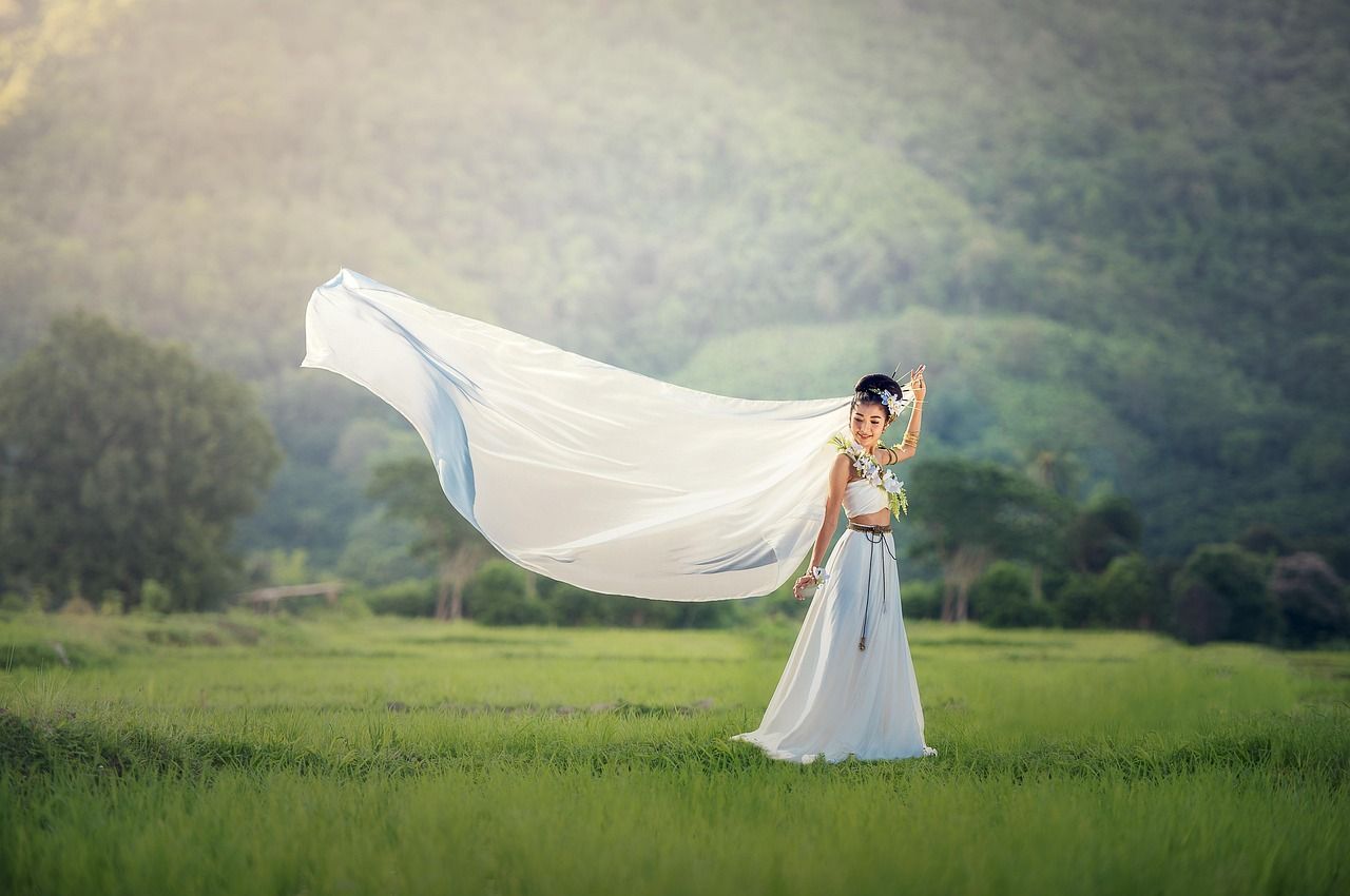 A flowing white dress billows in the wind as someone stands in a misty green meadow at sunrise.