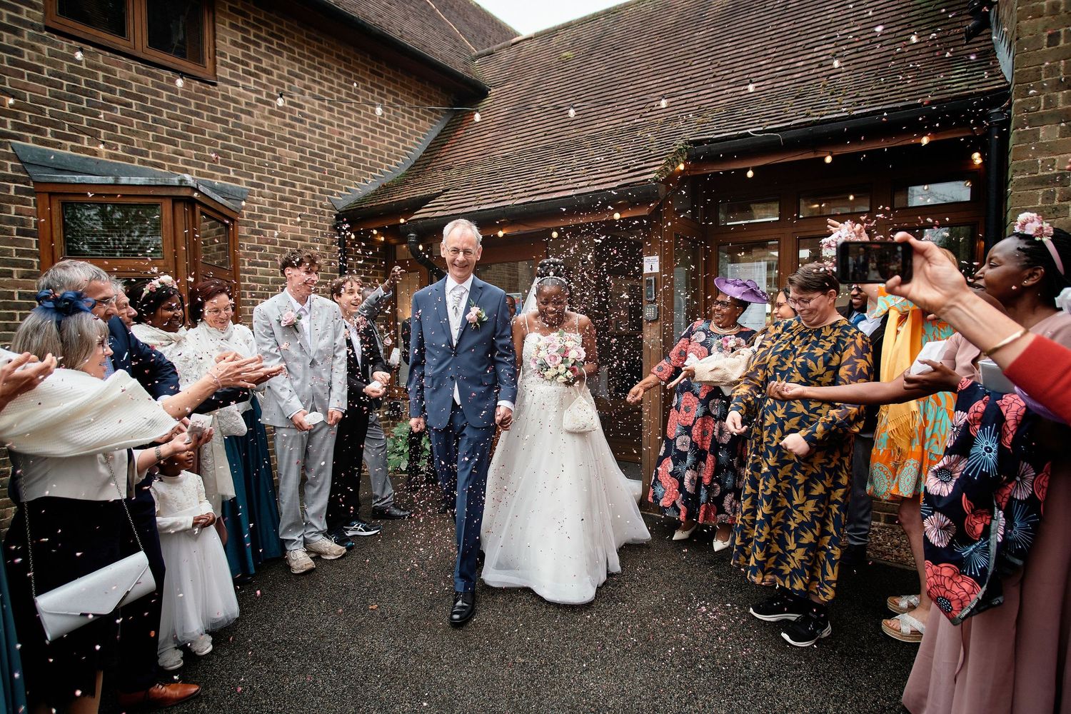 Guests blow bubbles and celebrate as newlyweds walk down brick pathway during outdoor wedding recessional.