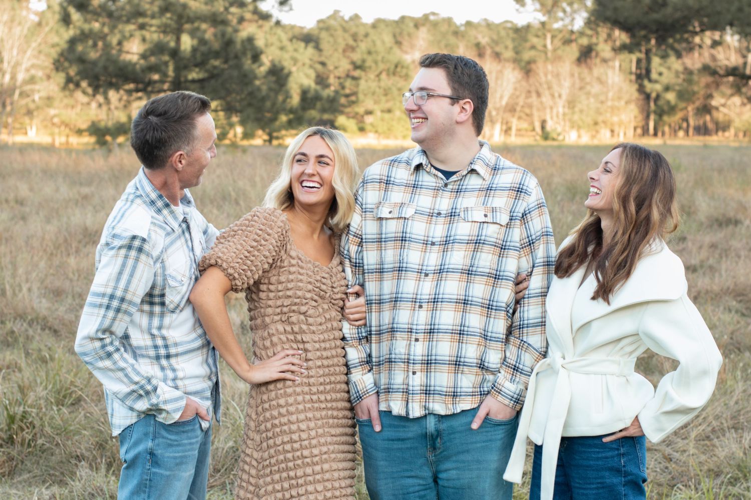 A group of four people laugh and smile together during a casual outdoor photoshoot.