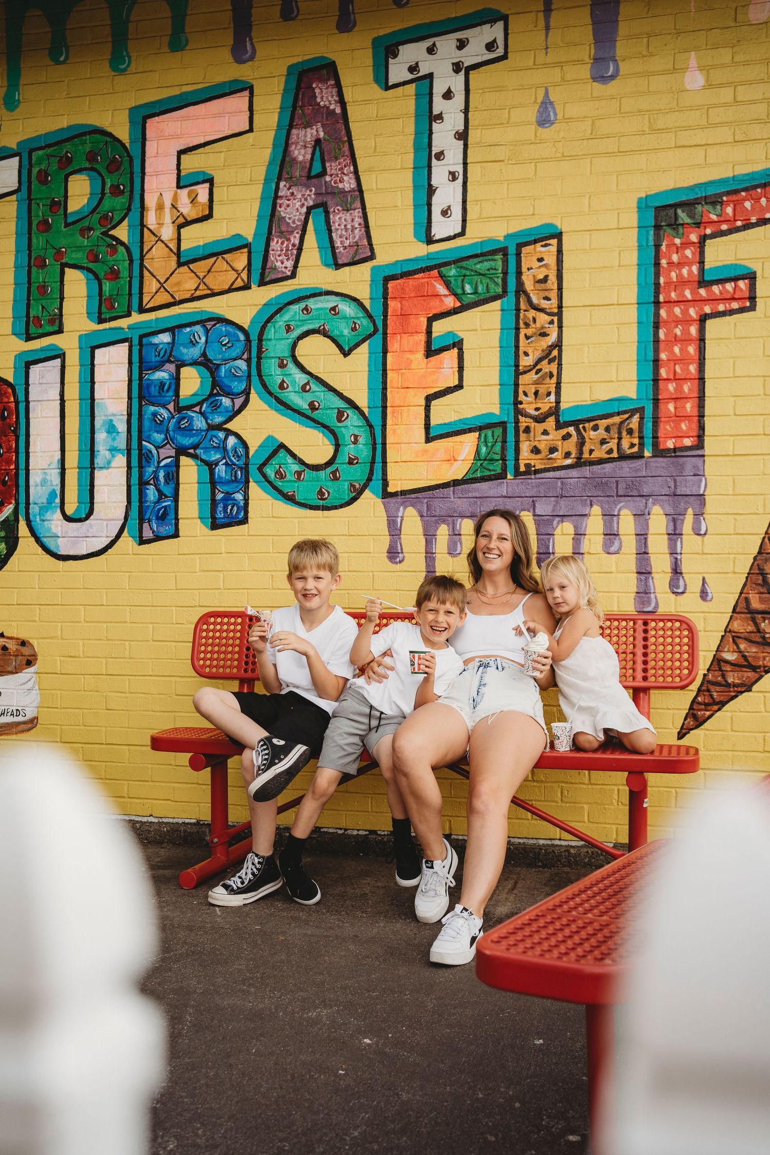 Group sits on red bench against colorful wall mural with text 'TREAT YOURSELF'.