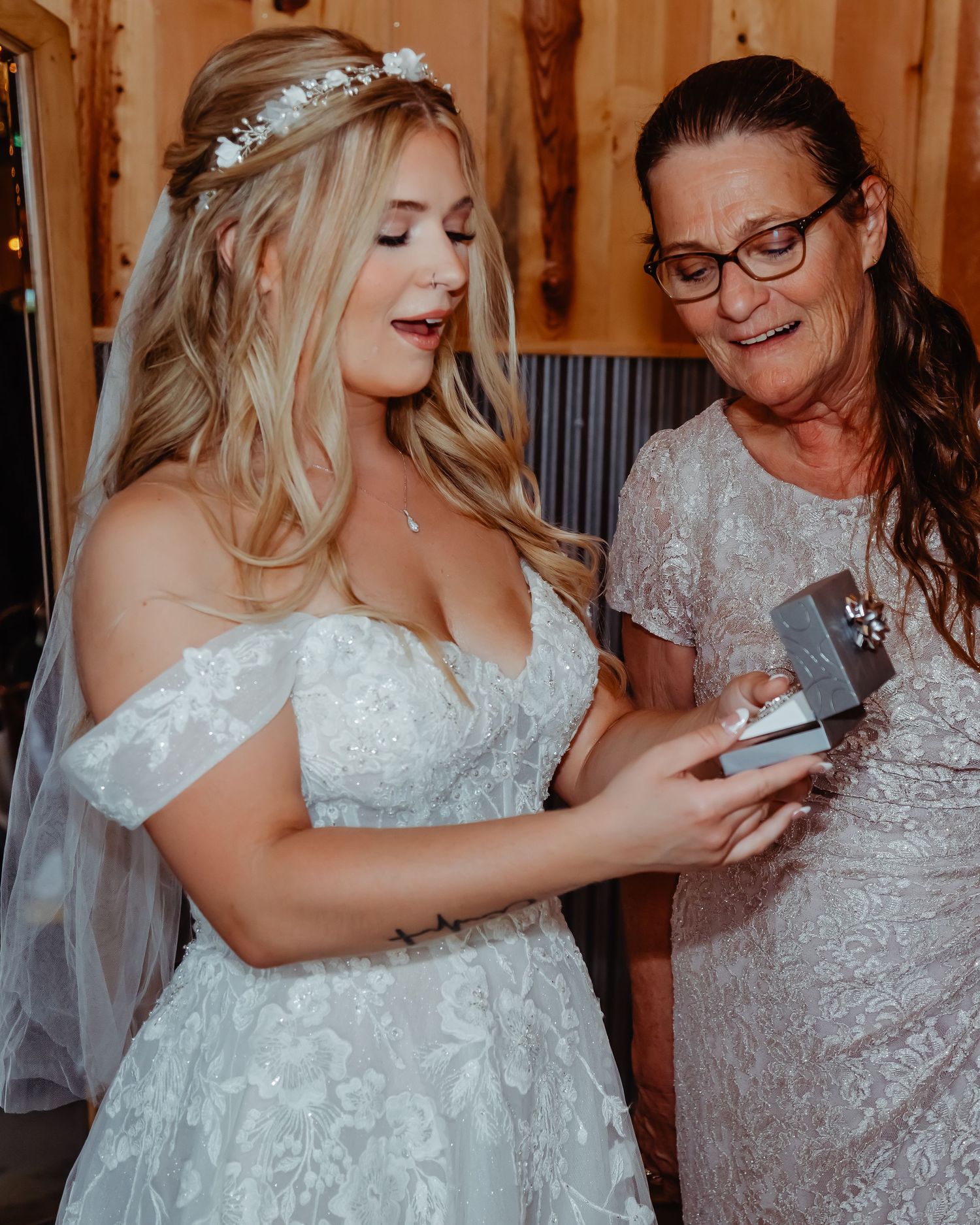 A bride in a white lace gown and crystal hairpiece shares an emotional moment while looking at a small item together.