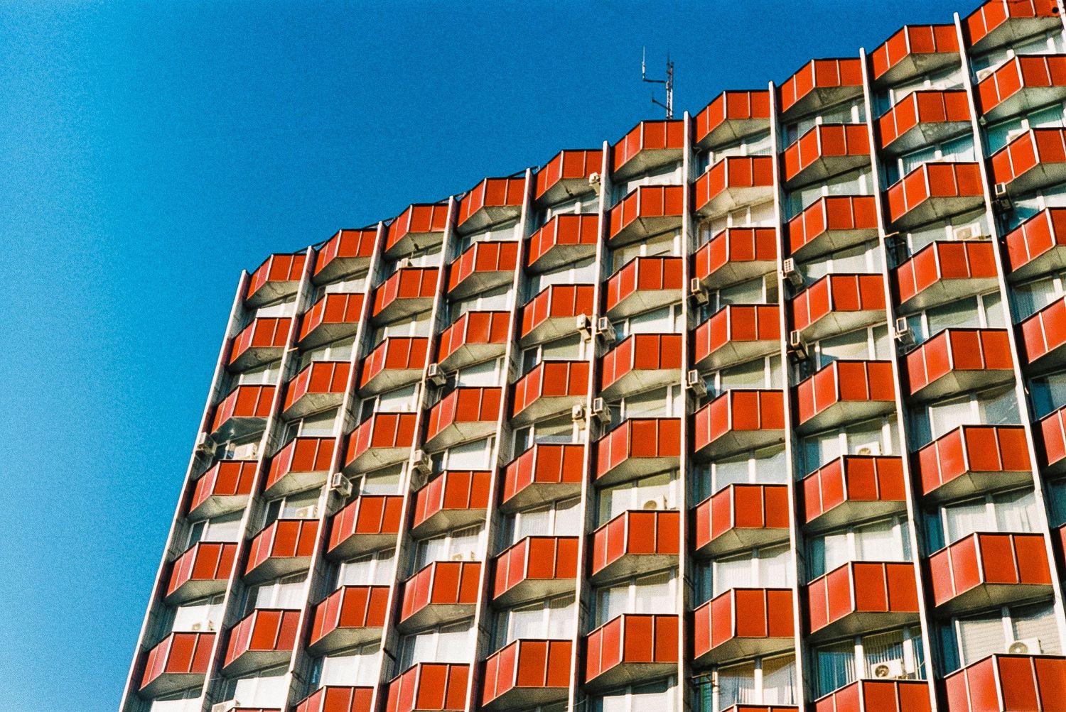 Orange and white geometric facade of a modernist apartment building against bright blue sky.