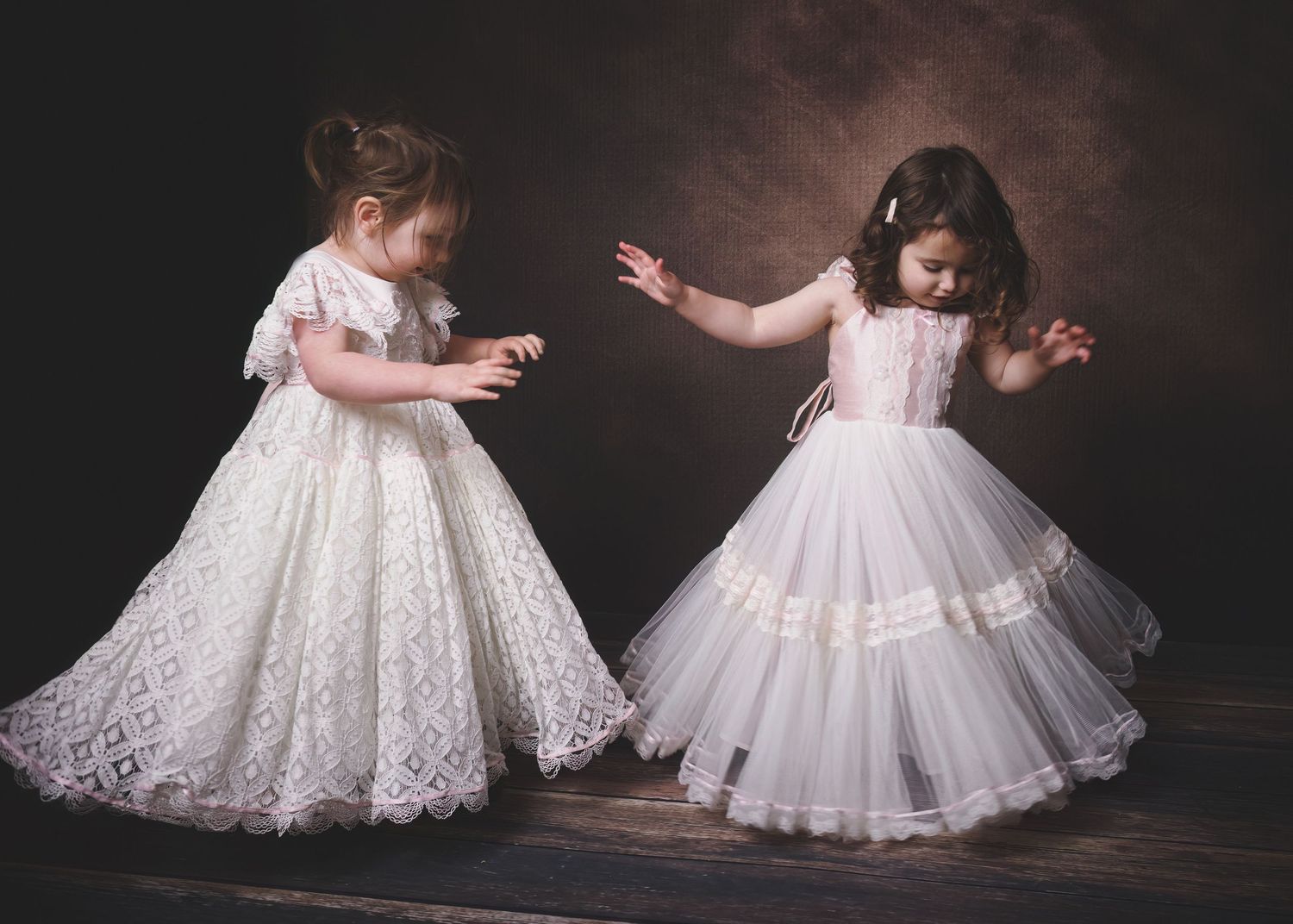 Portrait of two young children dancing in white gowns in a painterly style.