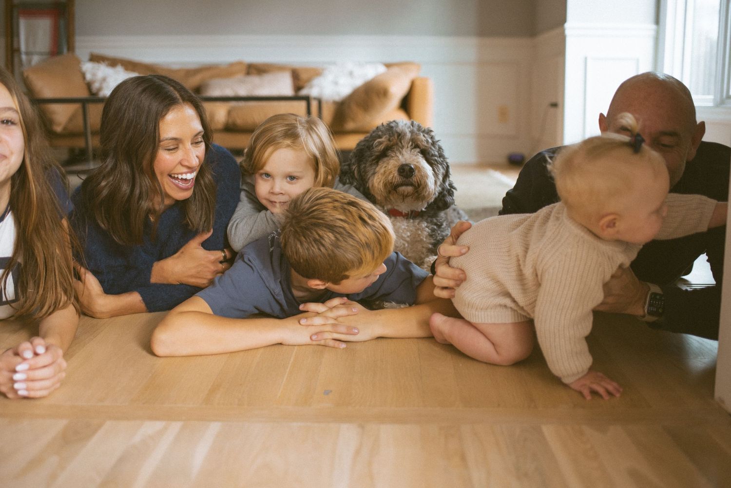 Group relaxing together on hardwood floor with a large German Shepherd dog in a cozy home setting.