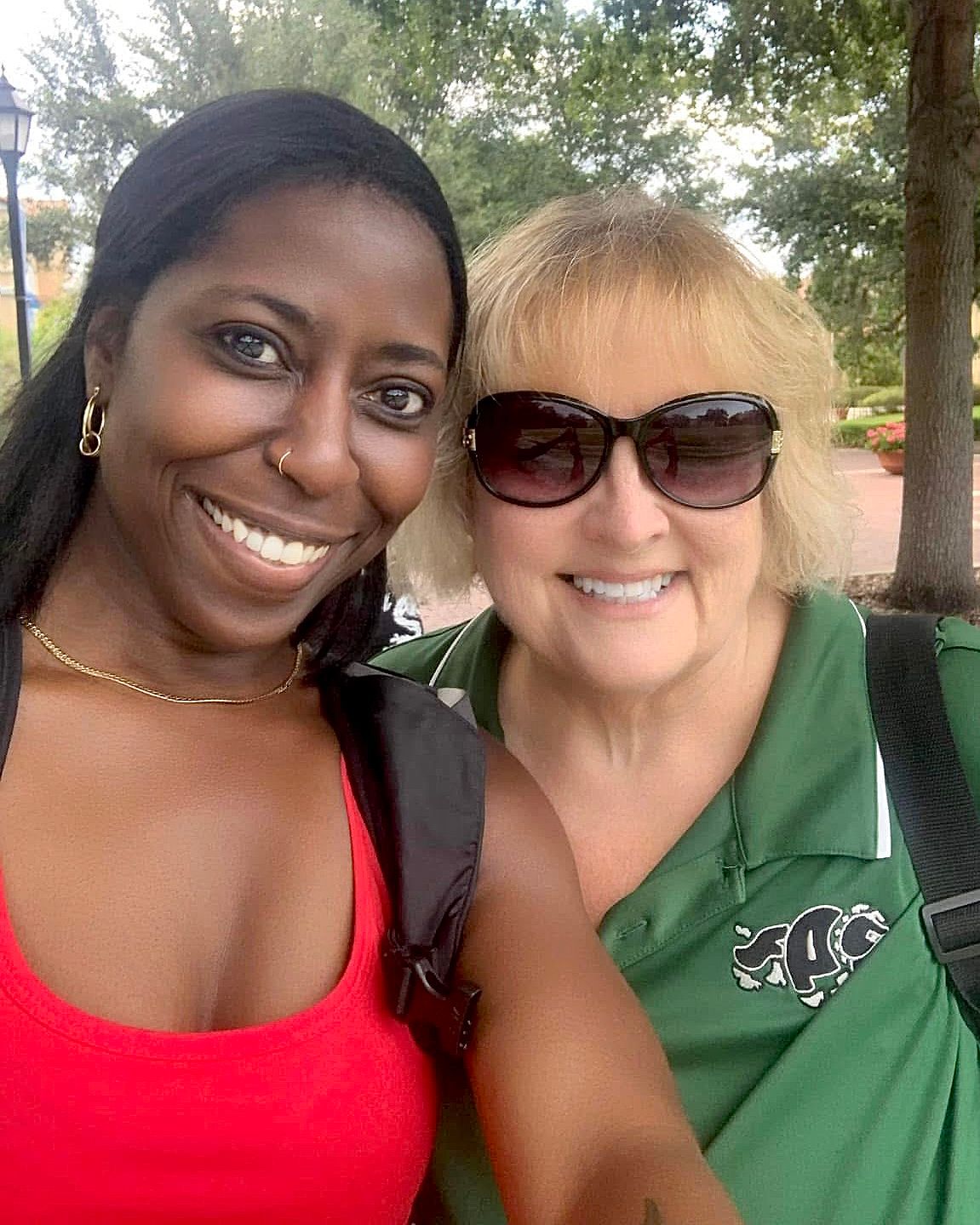 Vanessa, owner of VMS Photographs and her Kindergarten teacher smile together one wearing a red top and one in a green polo with sunglasses.