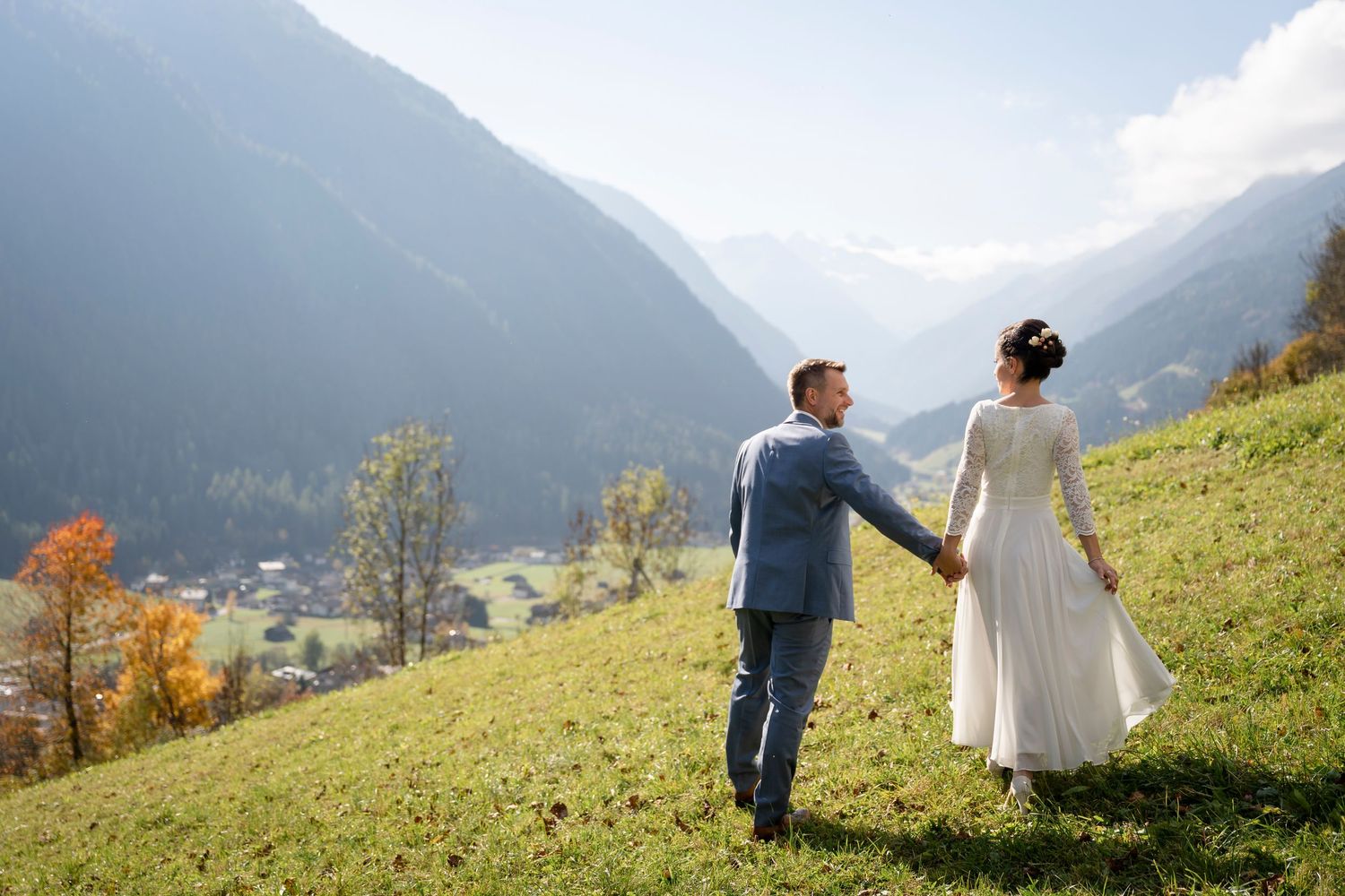 Brautpaar hält Hände auf einer Bergwiese mit Blick ins Tal