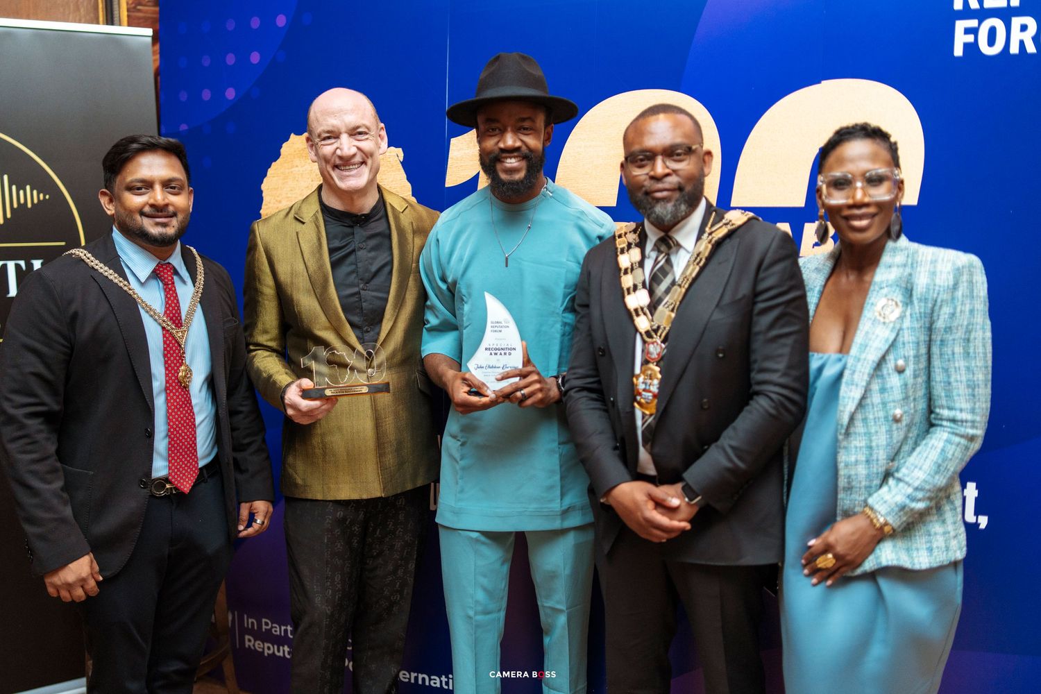 Five professionals pose together at an awards ceremony, with two holding trophy plaques, dressed in formal attire.