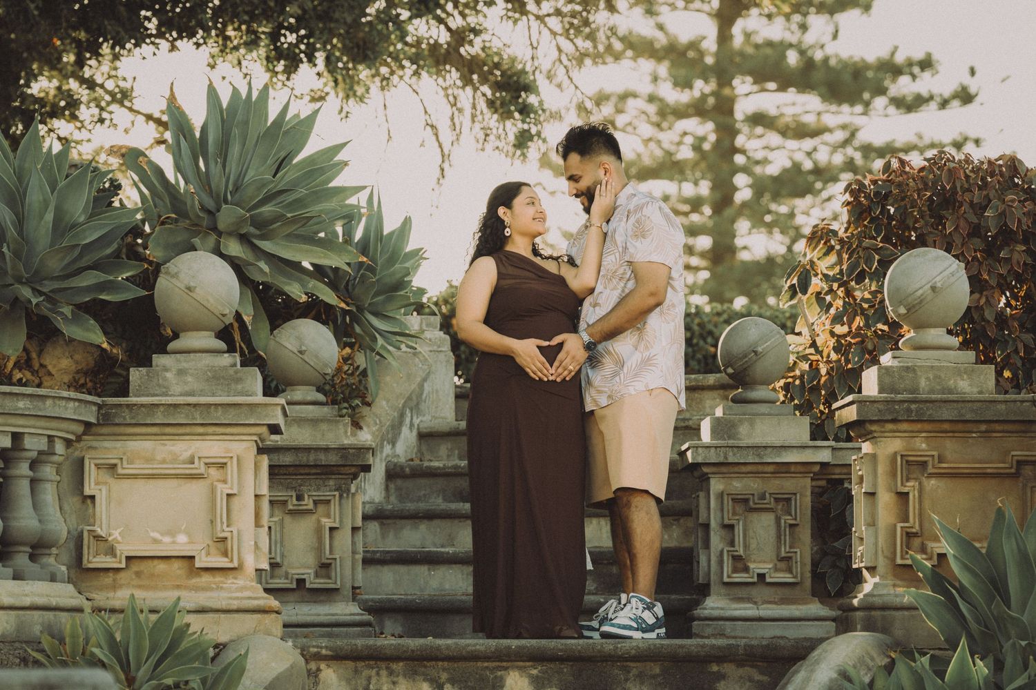 Pregnant couple embracing on stone steps surrounded by lush tropical gardens during a maternity photoshoot.