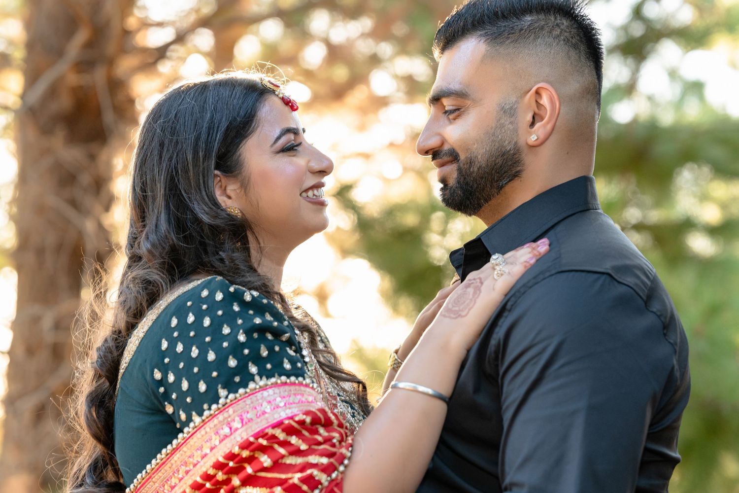 Indian couple in traditional attire sharing a romantic moment outdoors, woman in green and red saree, man in black shirt.