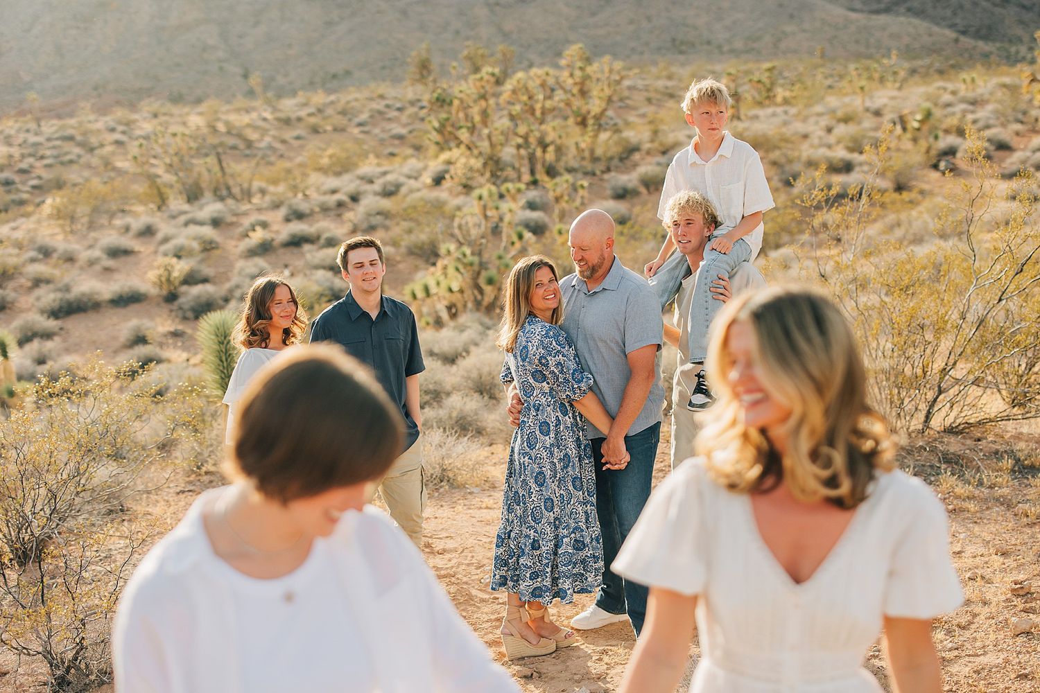 Family portrait session in desert landscape with Joshua trees, group of seven smiling in warm golden light.