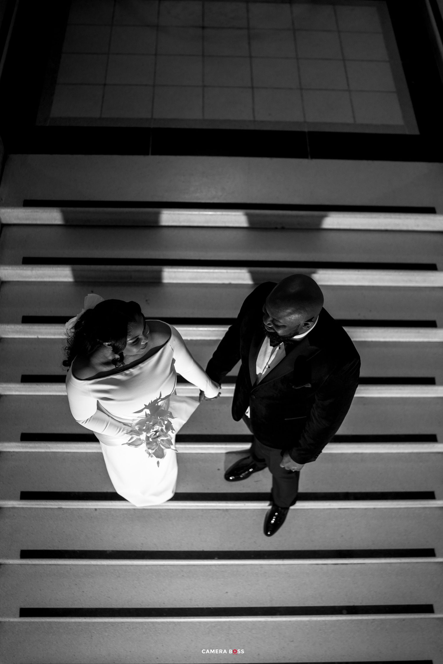 Black and white aerial photo of a bride and groom holding hands on elegant stairs at their wedding.