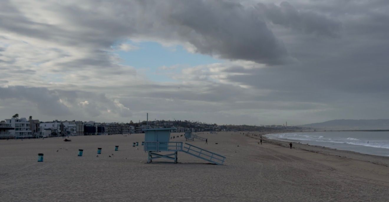 Overcast beach scene with a lifeguard stand on sandy shore, calm waves, and cloudy skies at Santa Monica Beach.