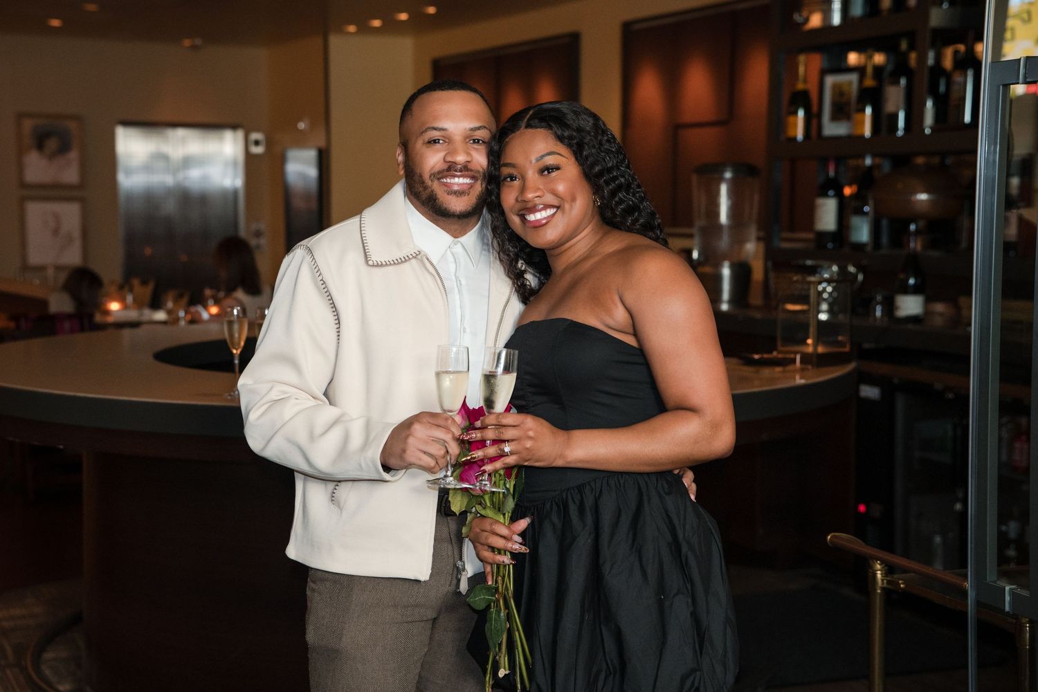 A couple in formal attire shares a joyful moment at an elegant bar setting with ambient lighting.