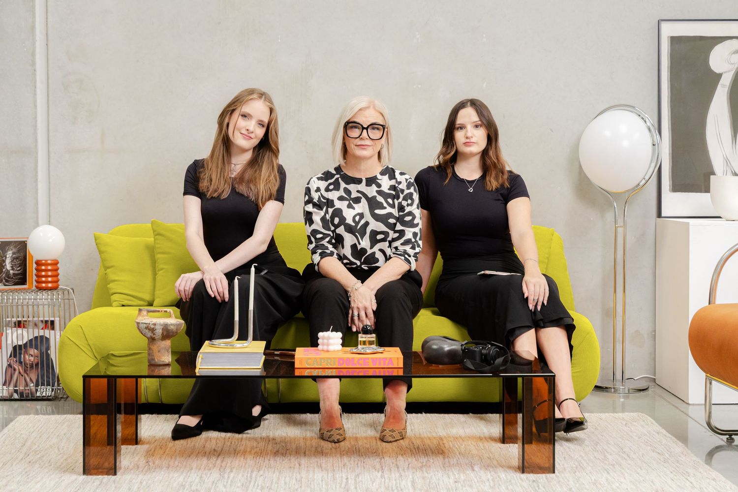 Three people sit on a modern gray couch in a bright living room with colorful accents and decor.