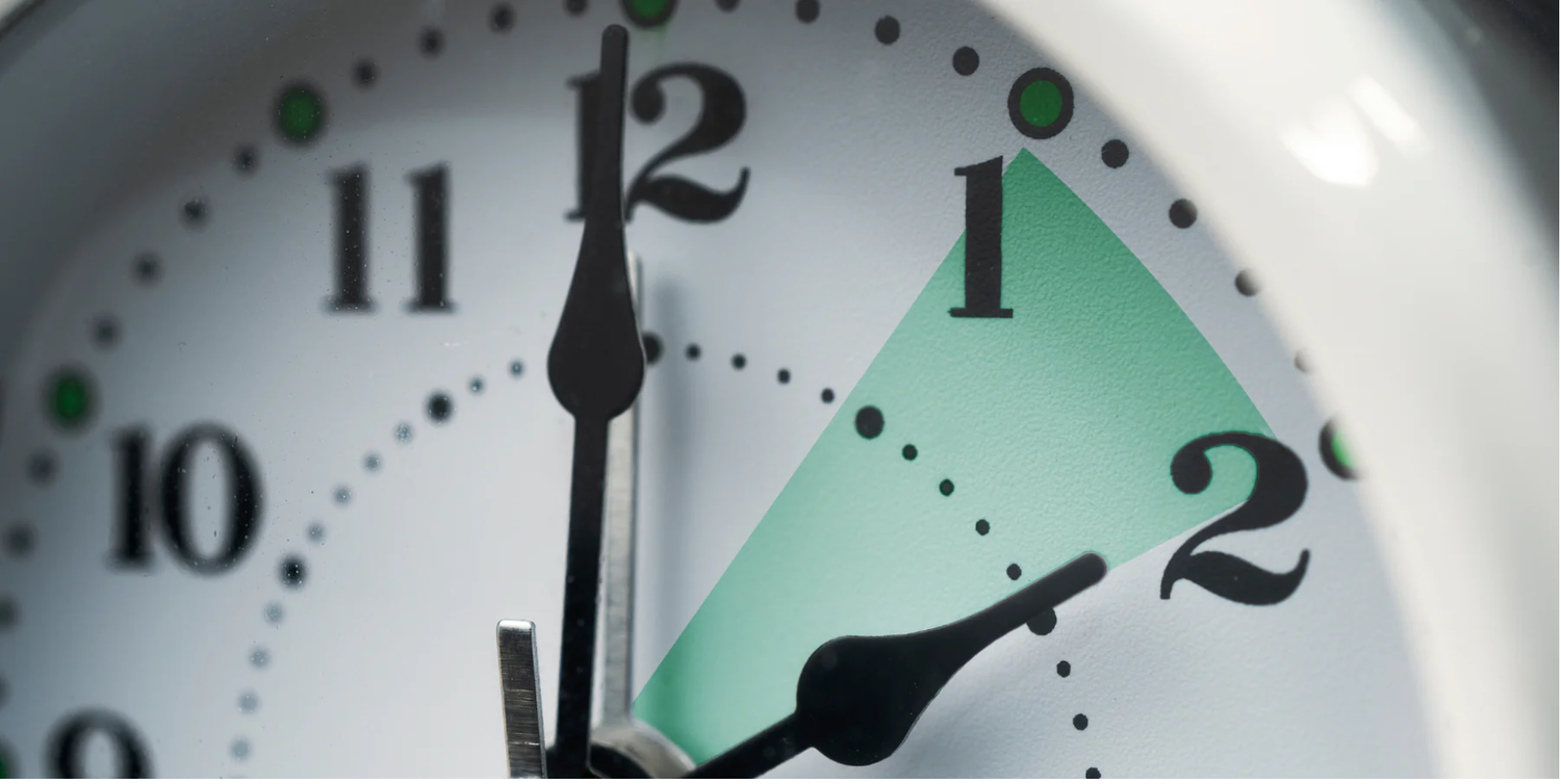 Close-up of a white analog clock face showing time near 1:10 with green triangle highlight between hands.