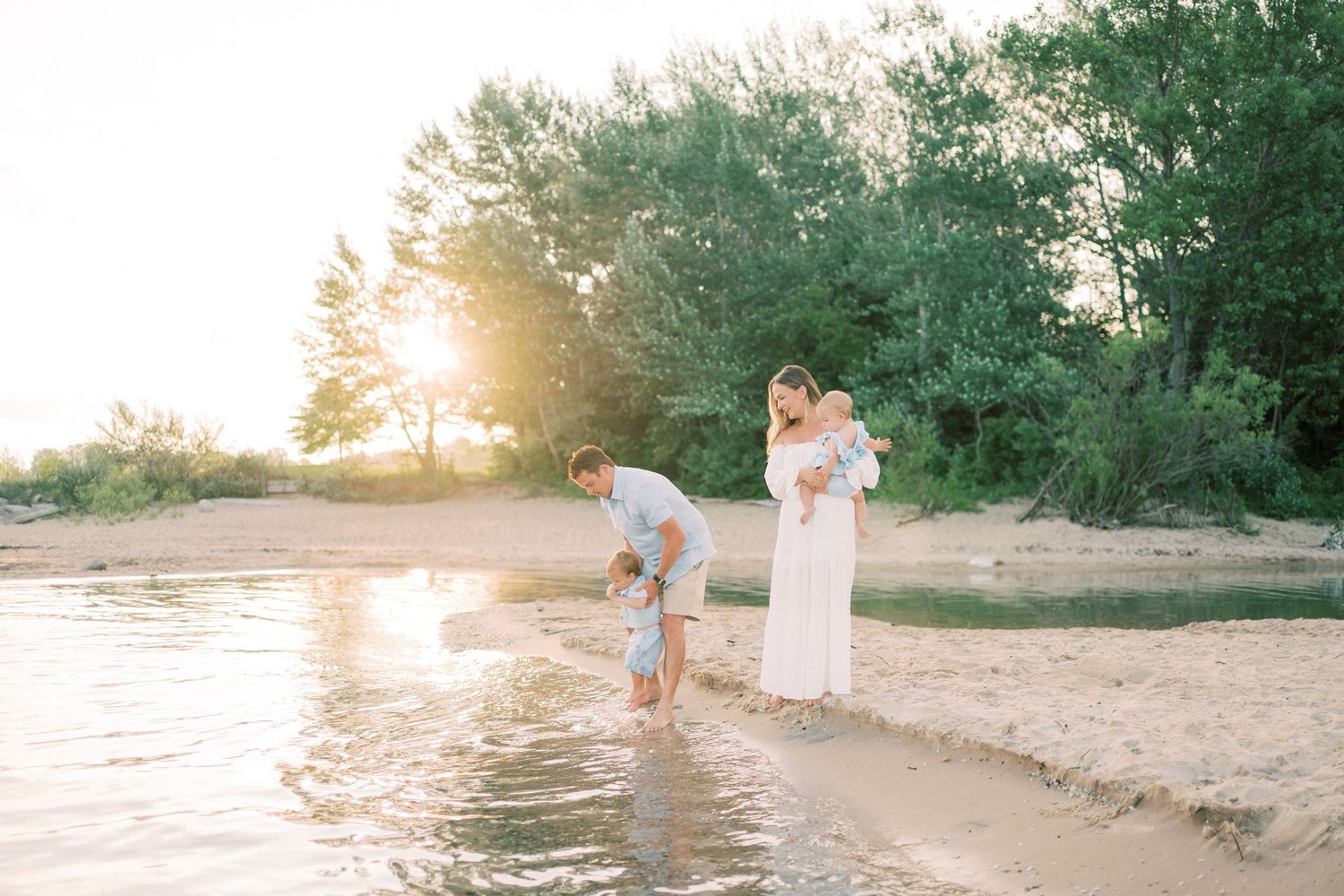 Family with young children playing at water's edge on sandy beach during golden sunset.