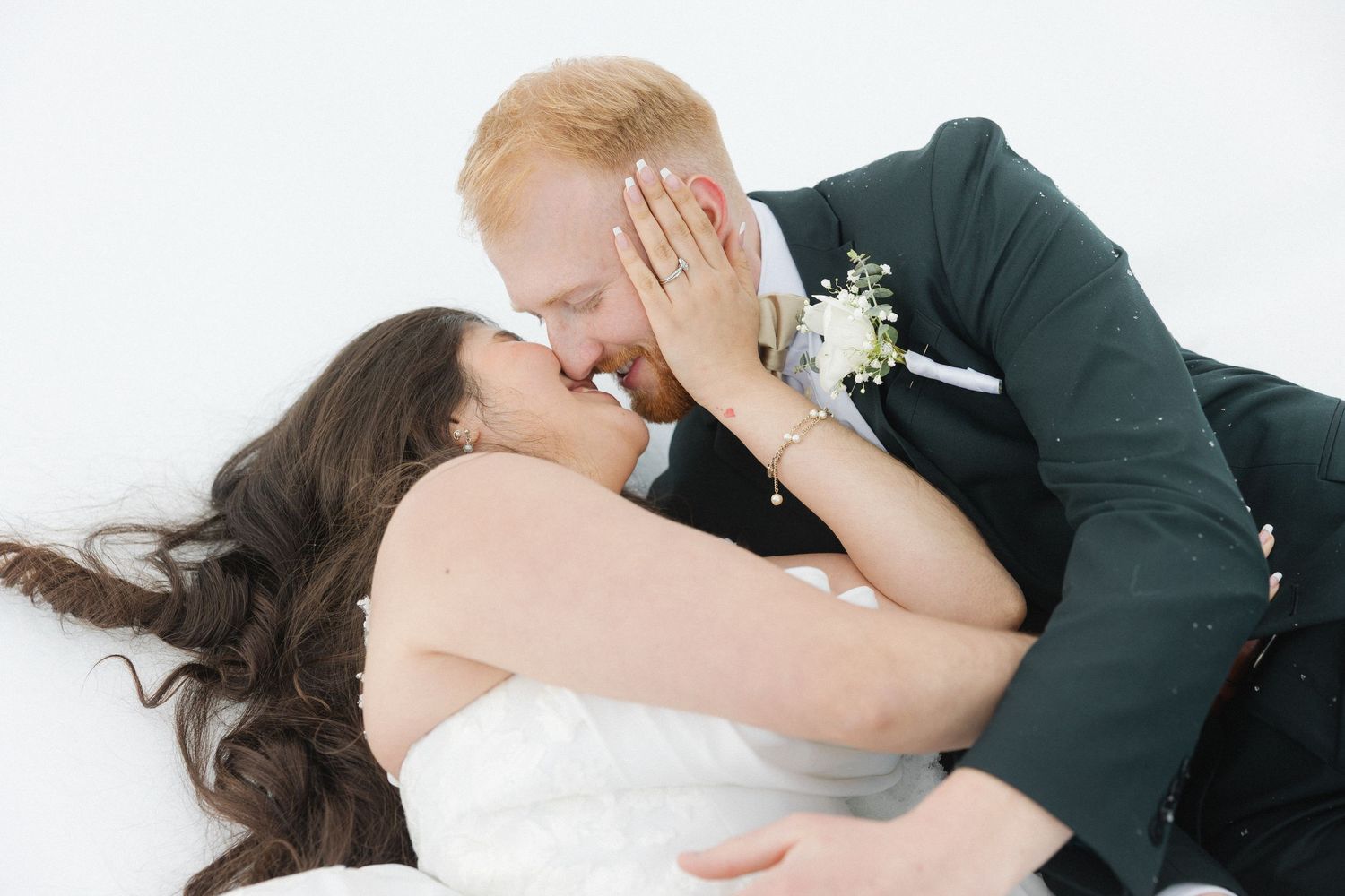 Couple sharing a romantic kiss in a snowy mountain winter wedding setting, groom in dark suit with boutonniere.