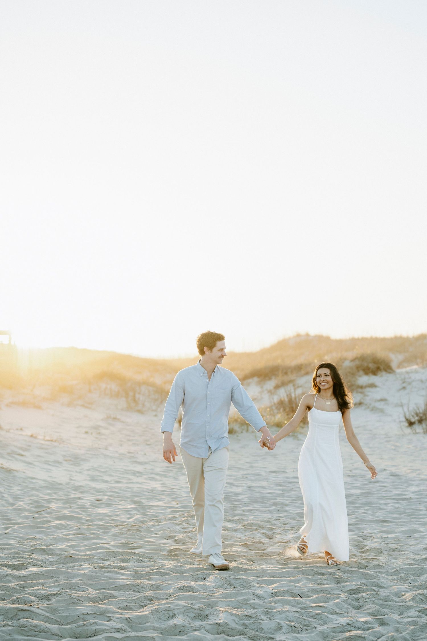A couple shares a romantic sunset kiss on the beach, with golden backlight glowing between them.